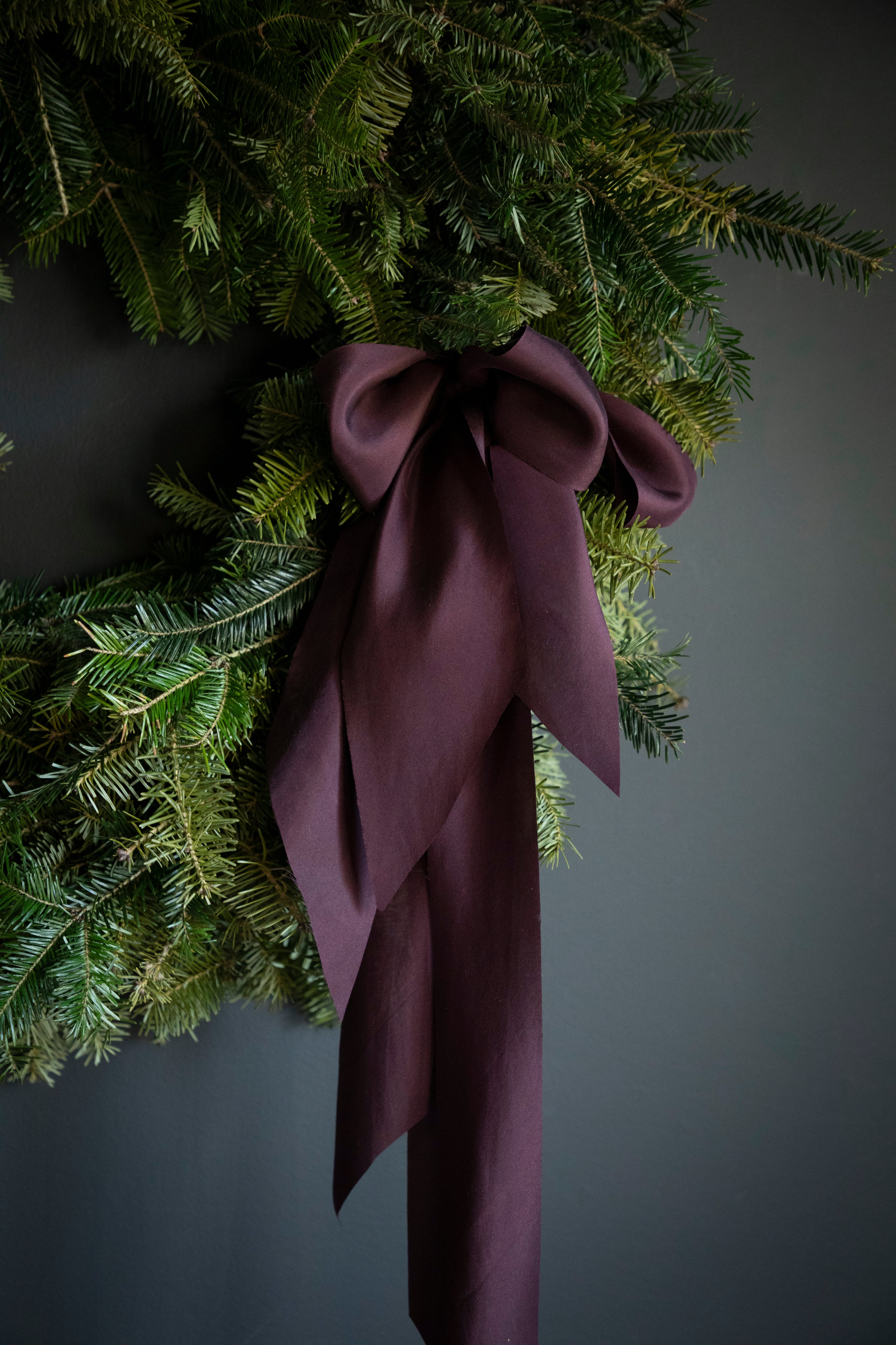 handmade holiday wreath made of evergreens. moody elegance with prple silk ribbons