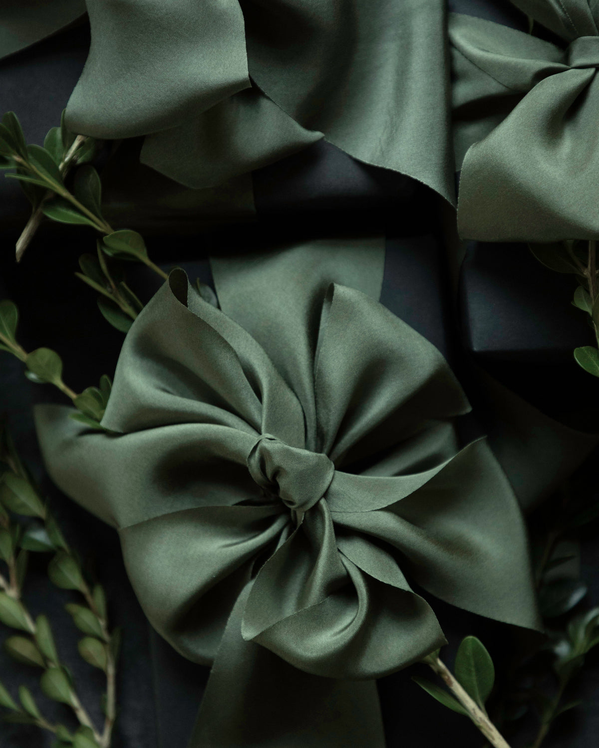 Olive green satin ribbon bows arranged on a dark background with green foliage accents.