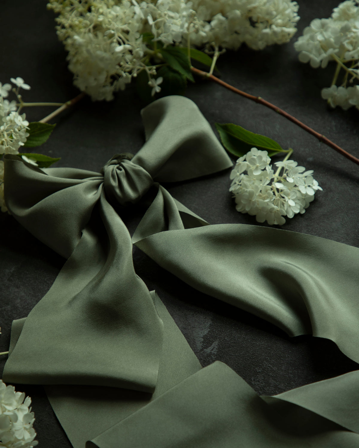 Green fabric with a bow and white flowers on a dark surface