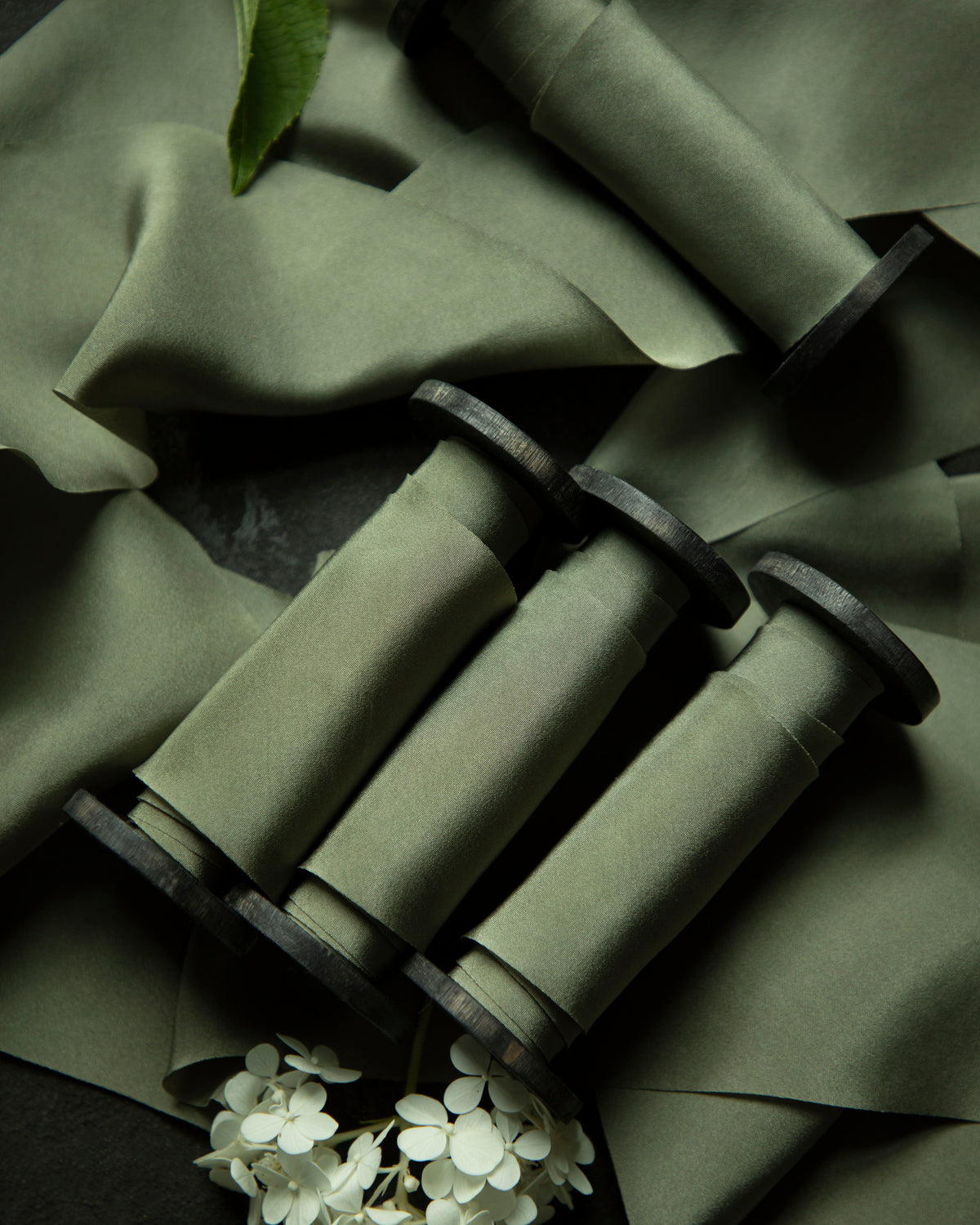 Green fabric with rolled-up items and white flowers on a dark background