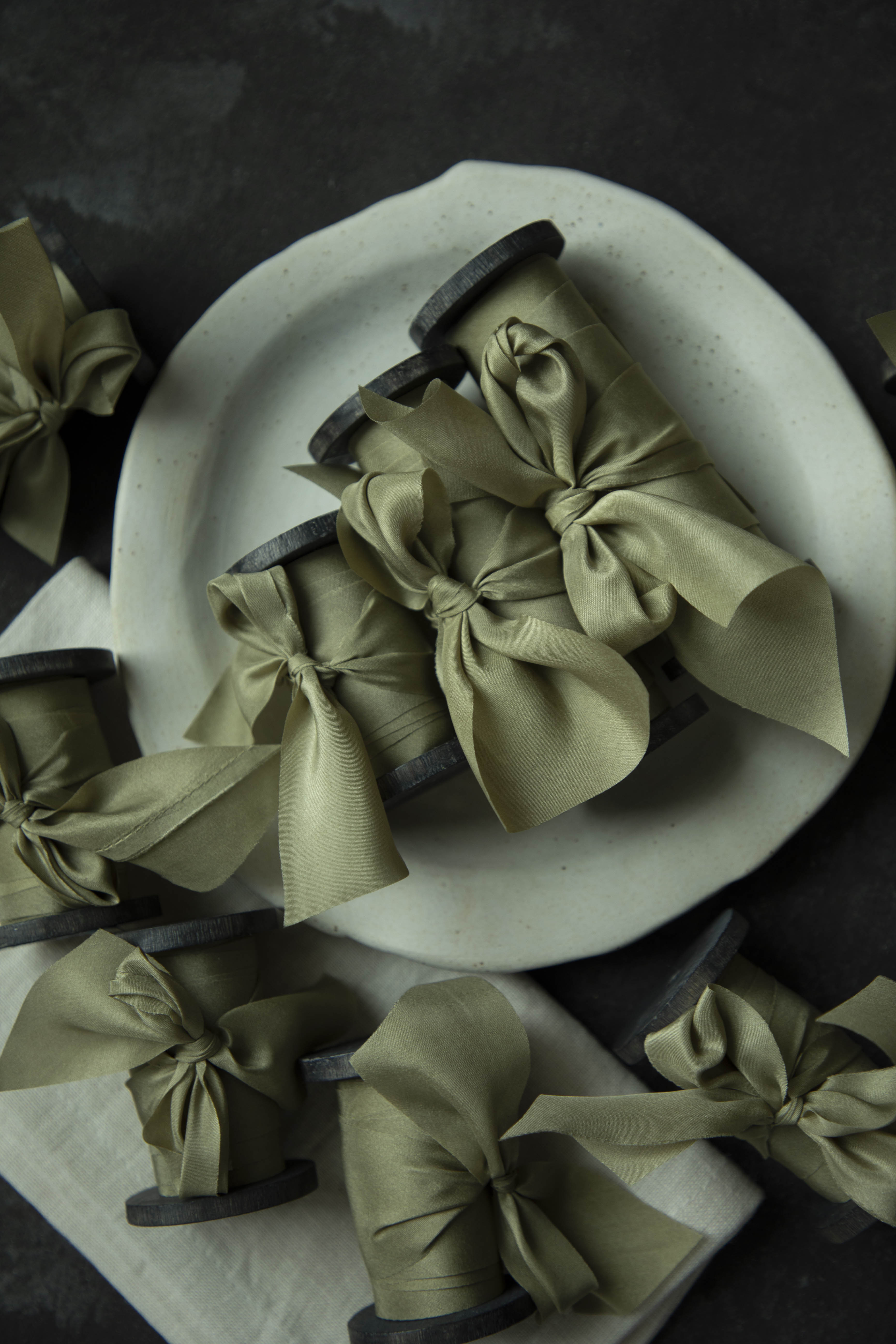 Green ribbons tied into bows on wooden spools with a white plate in the background.