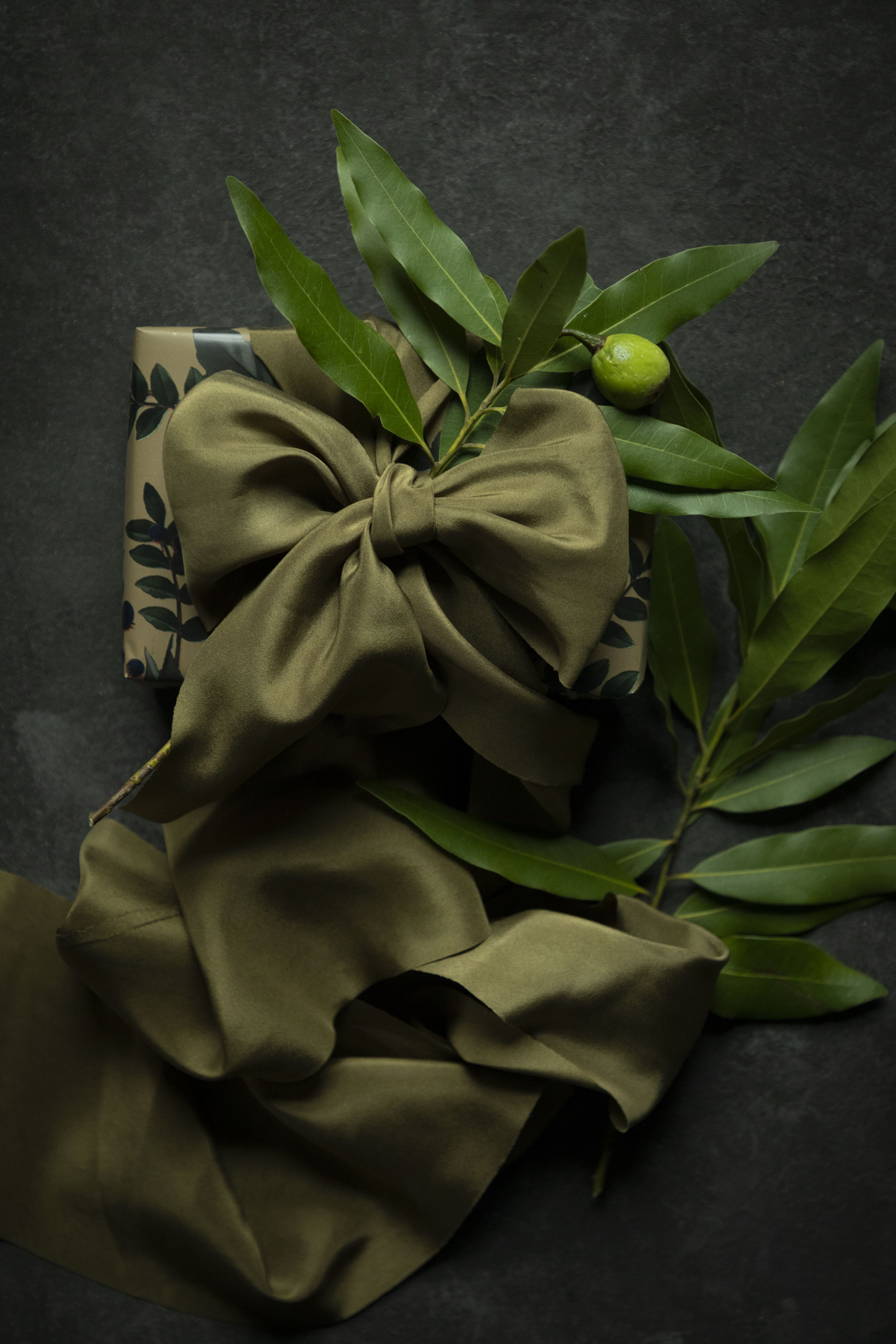 Gift wrapping inspiration with green ribbon with a bow on a gift box and leaves on a dark background