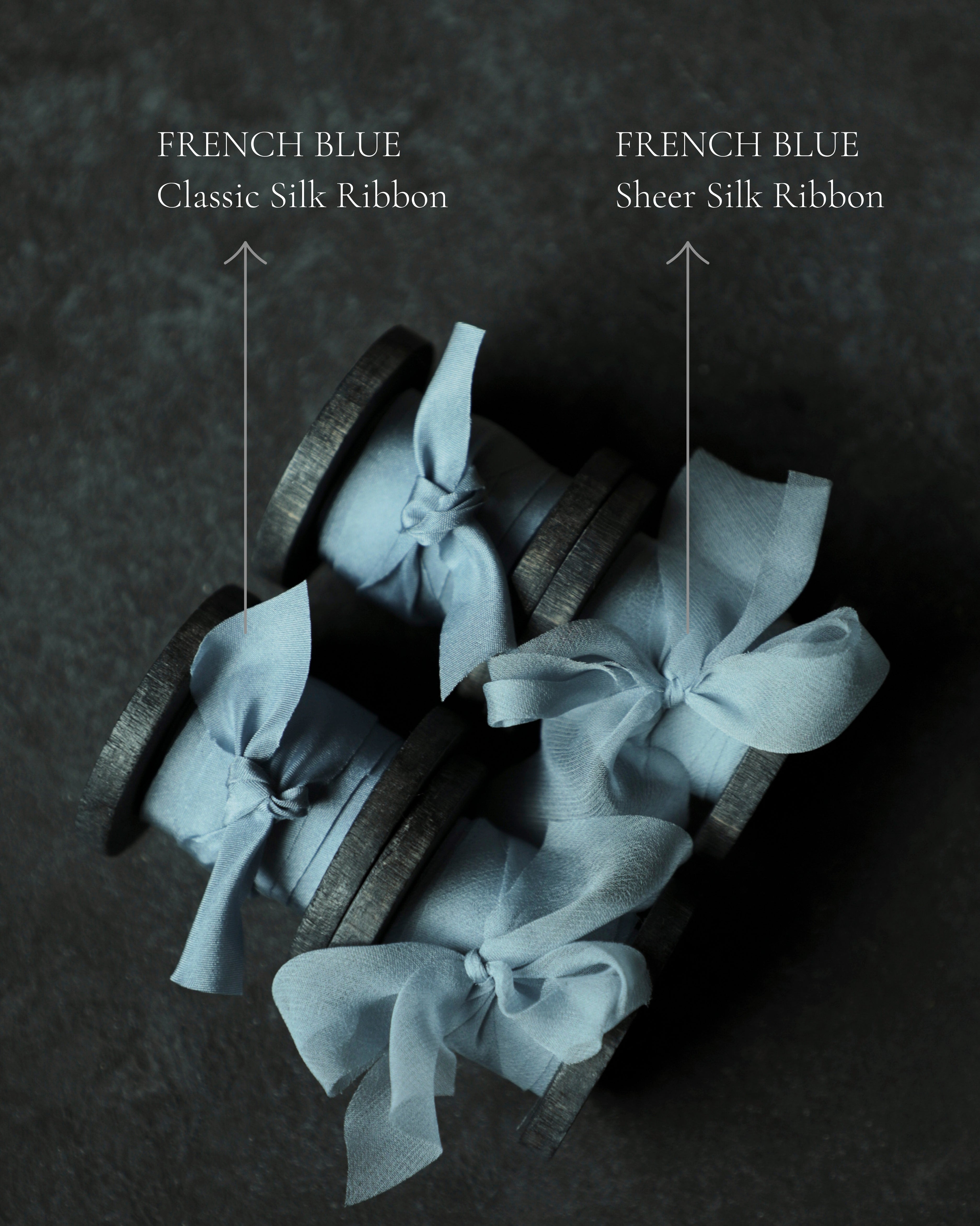 Three wood spools wrapped in pale blue sheer silk ribbon bows, arranged on a dark textured surface.