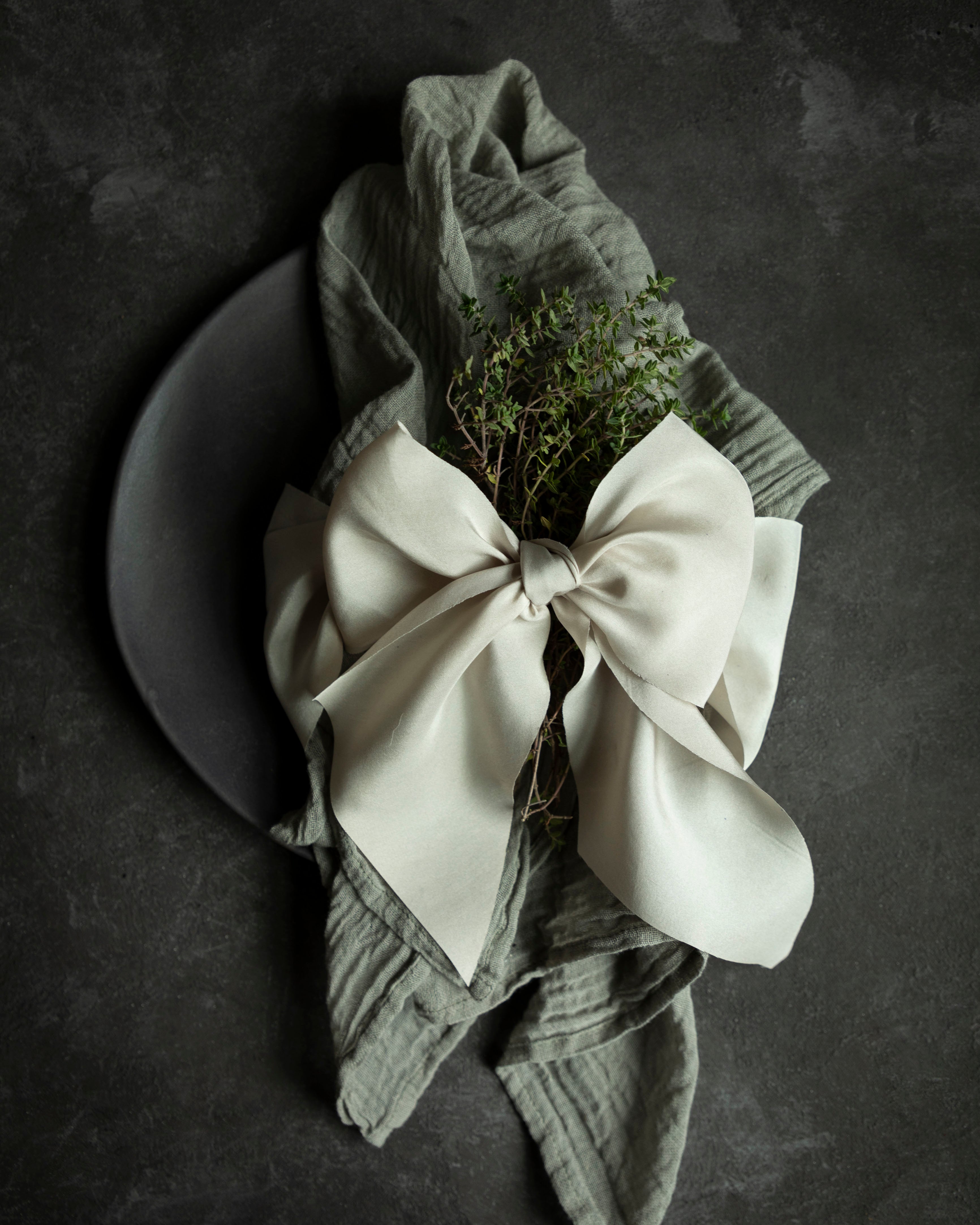 Eco-friendly wedding decor featuring gray cotton napkins on a placesetting tied with a champagne color ribbon bow. Hand-loomed and plant dyed cotton napkins.