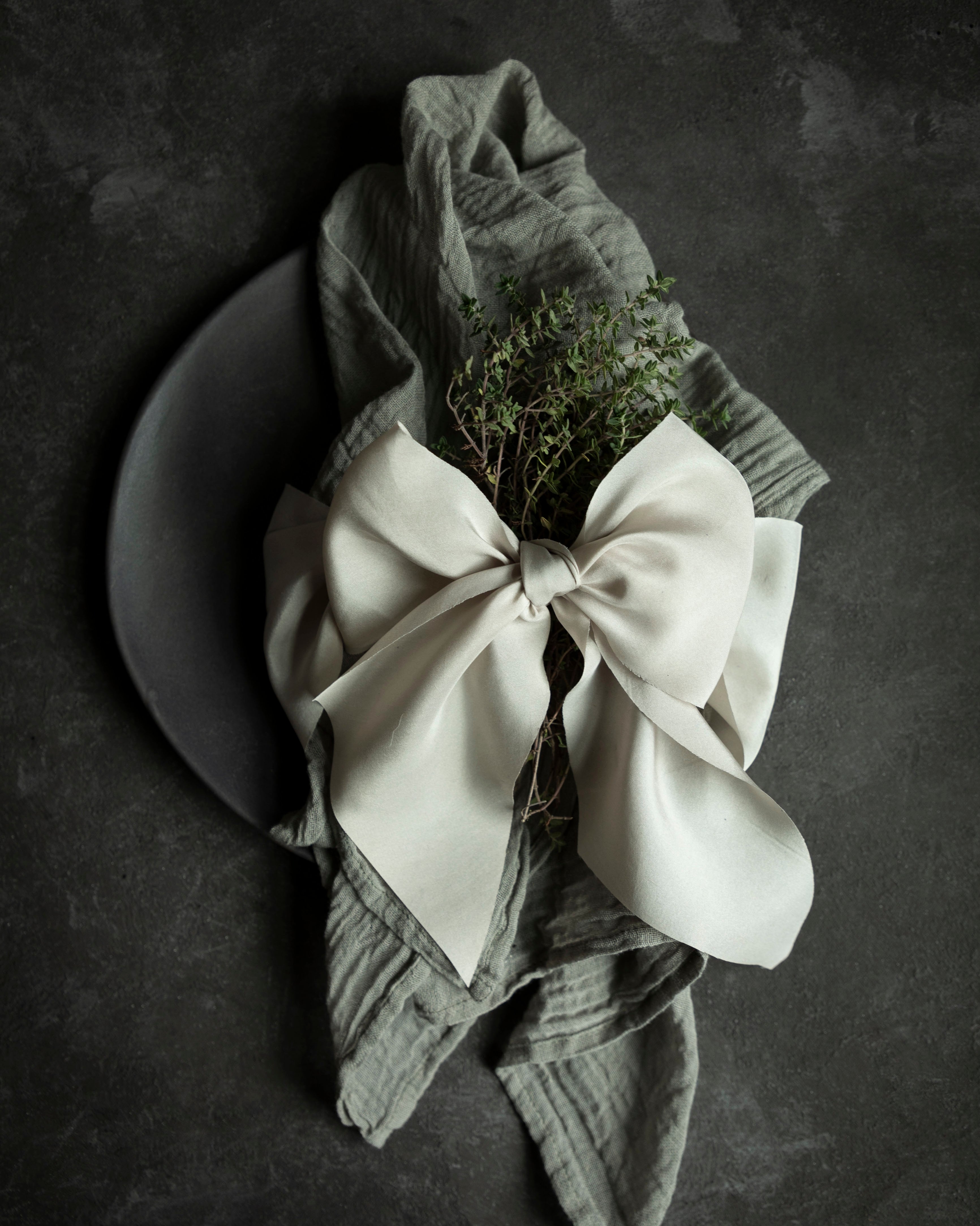 Folded napkin with a white bow and greenery on a dark surface