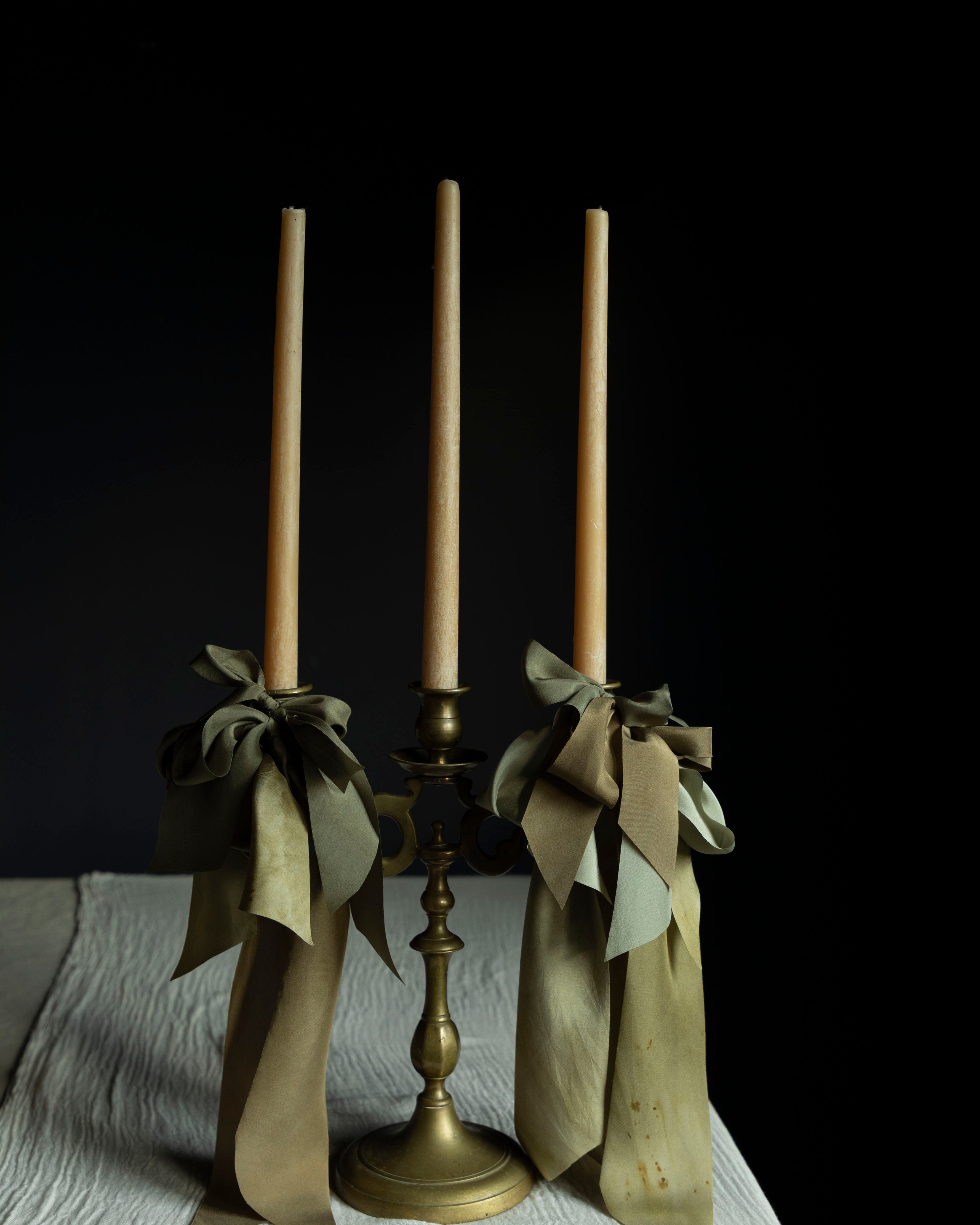 Brass candle holder with three candles and ribbons on a dark background