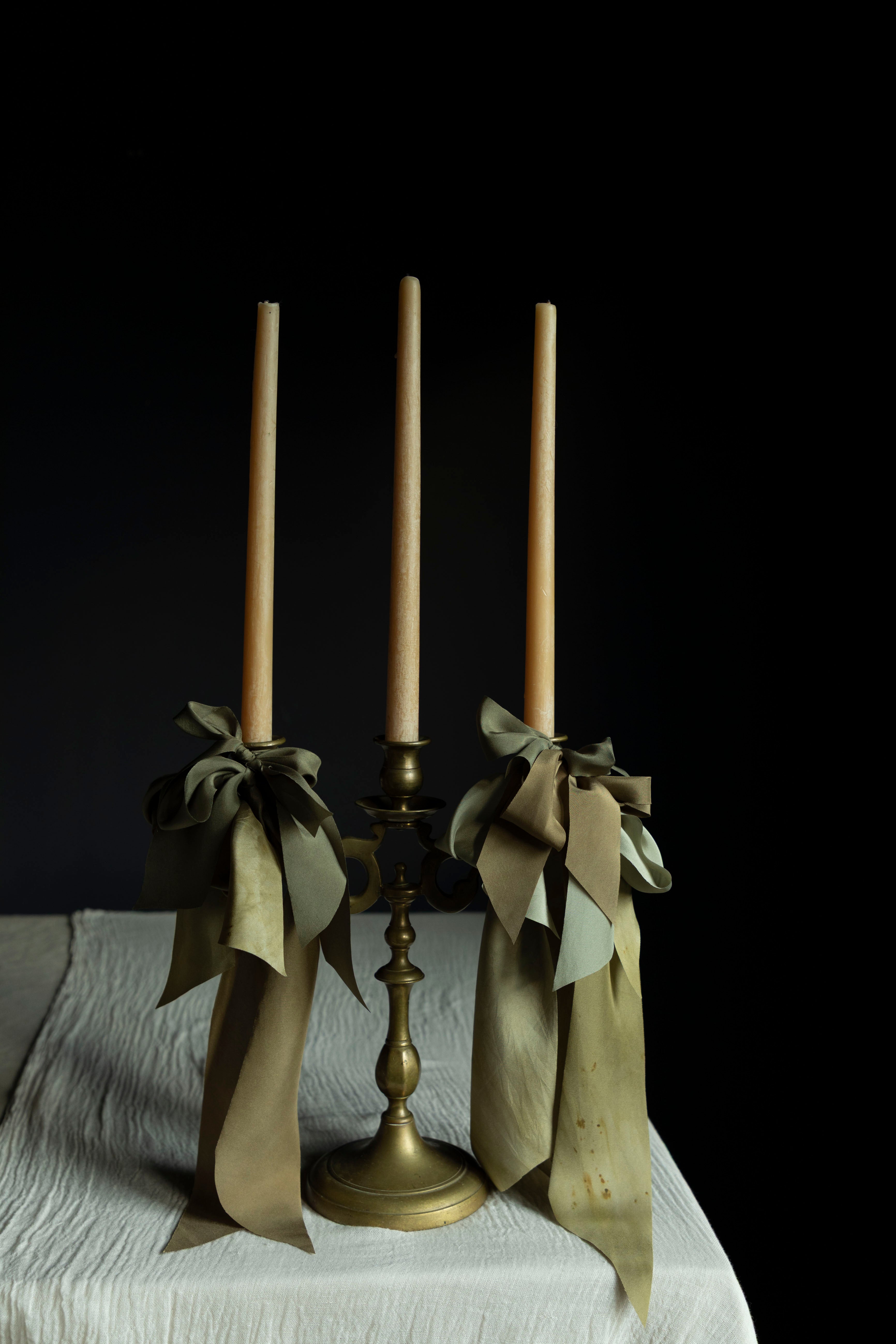 Brass candle holder with three candles and ribbons on a dark background
