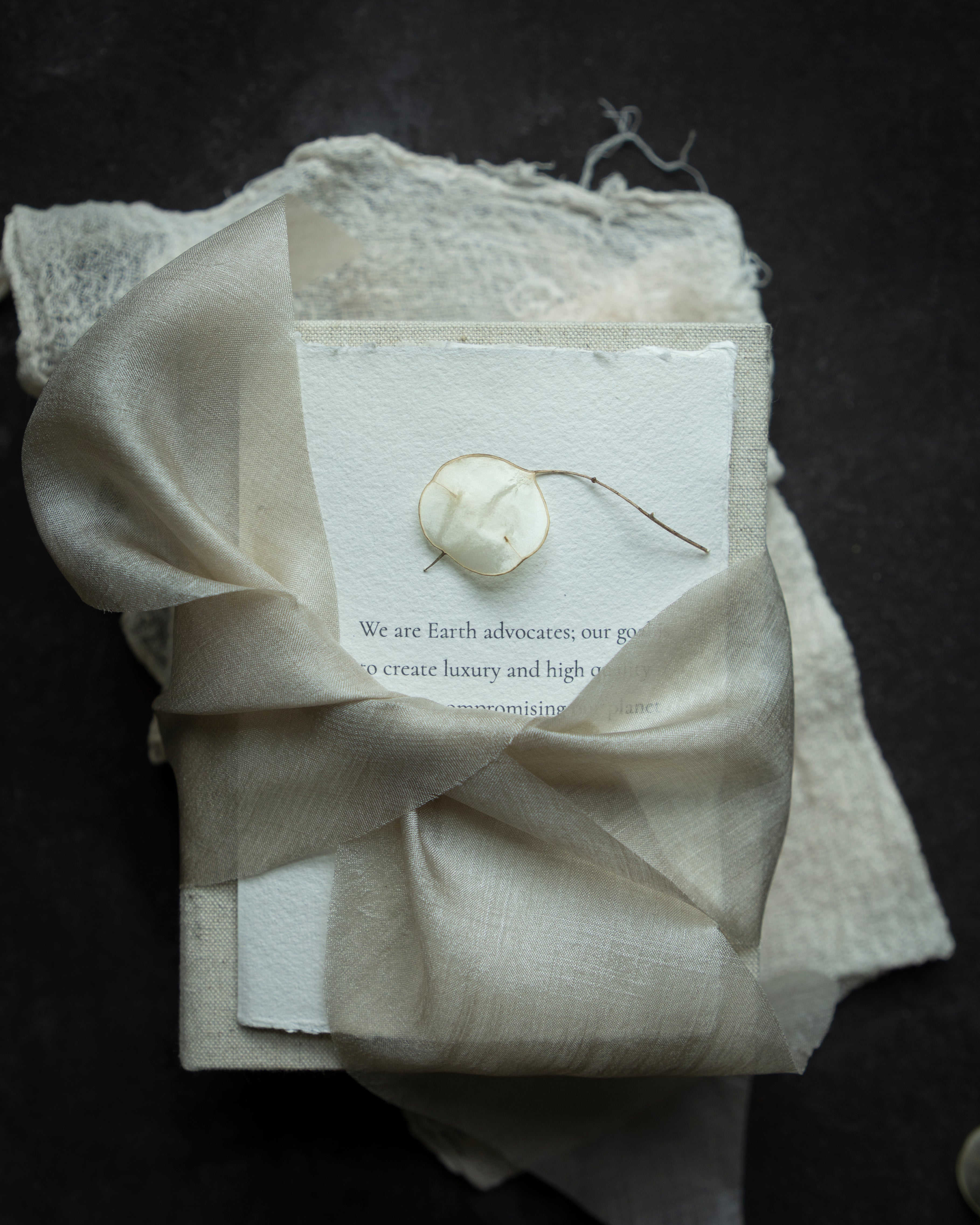 Neatly folded beige fabric with a dried plant and card on a dark background