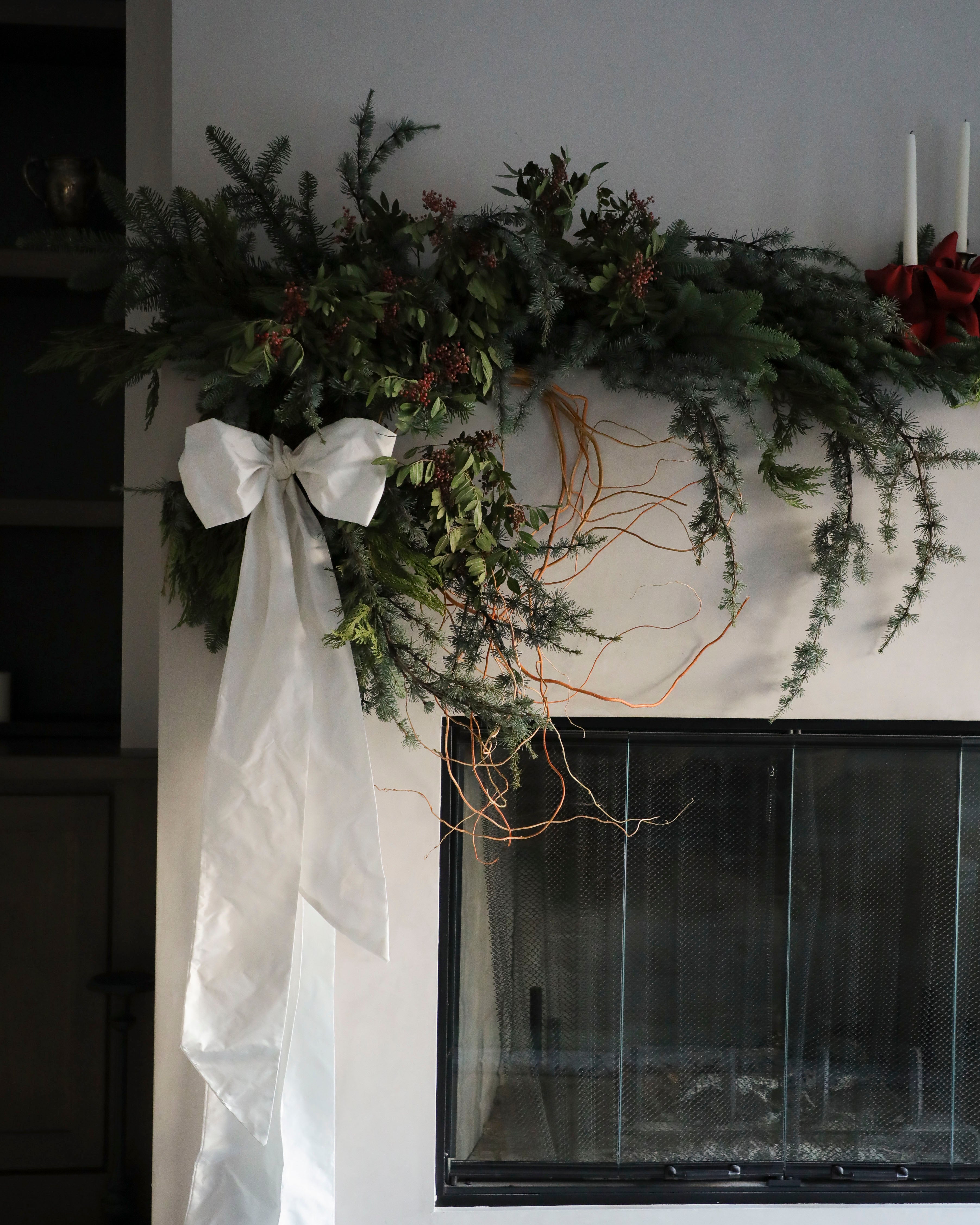Decorative greenery on a mantel with a white ribbon and a fireplace in the background.
