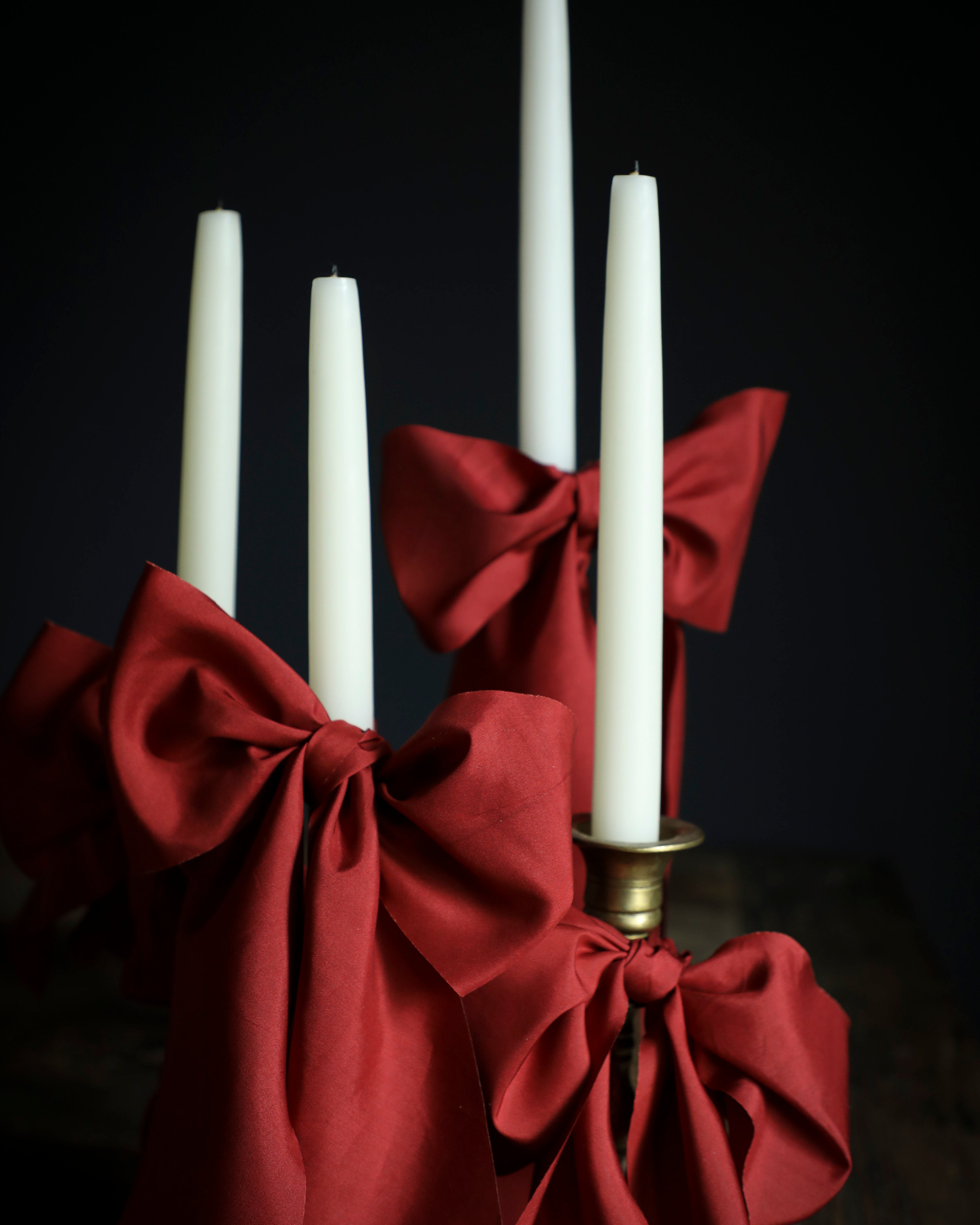 Candle holder with red ribbon and white candles against a dark background