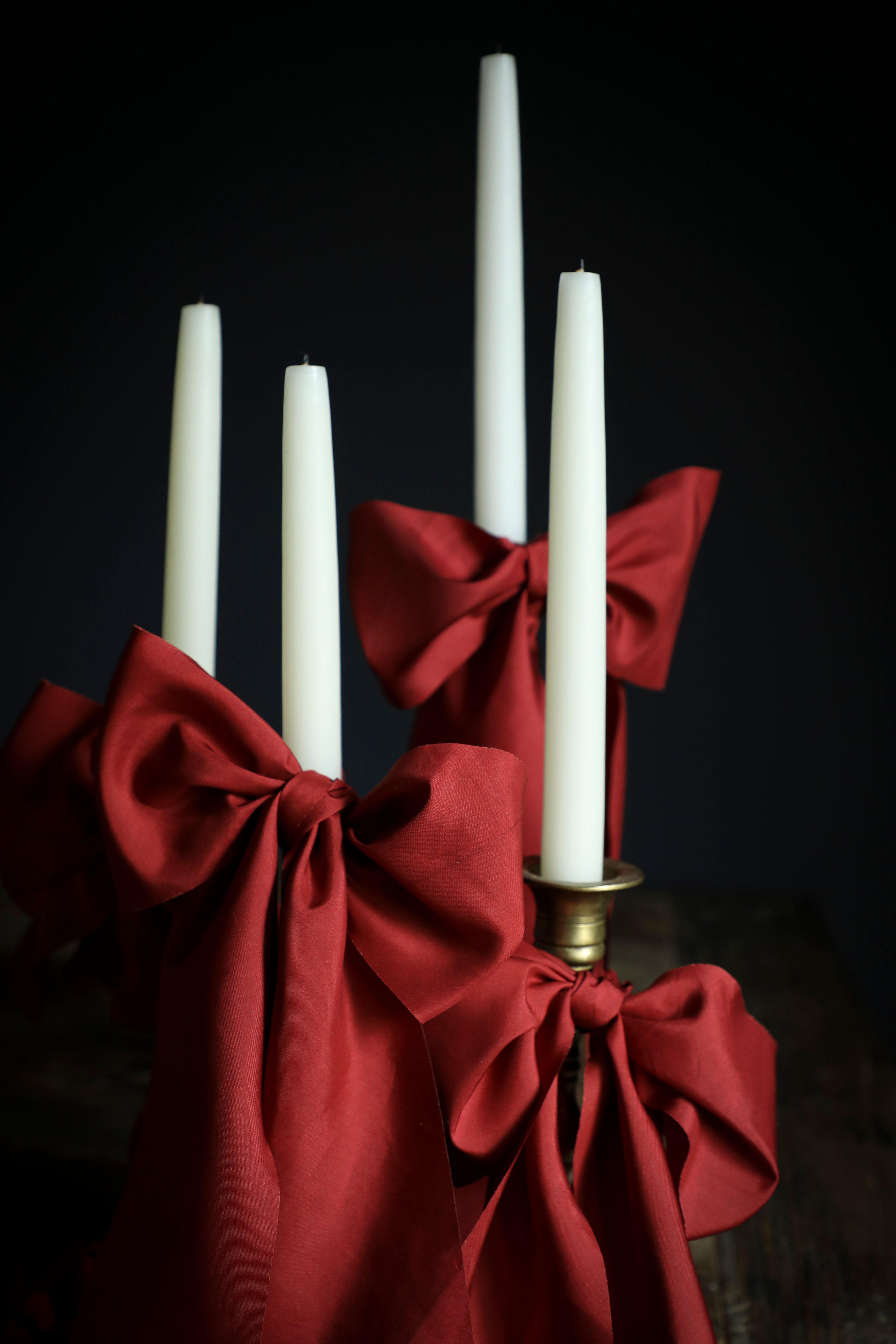 Candle holder with red ribbon and white candles against a dark background