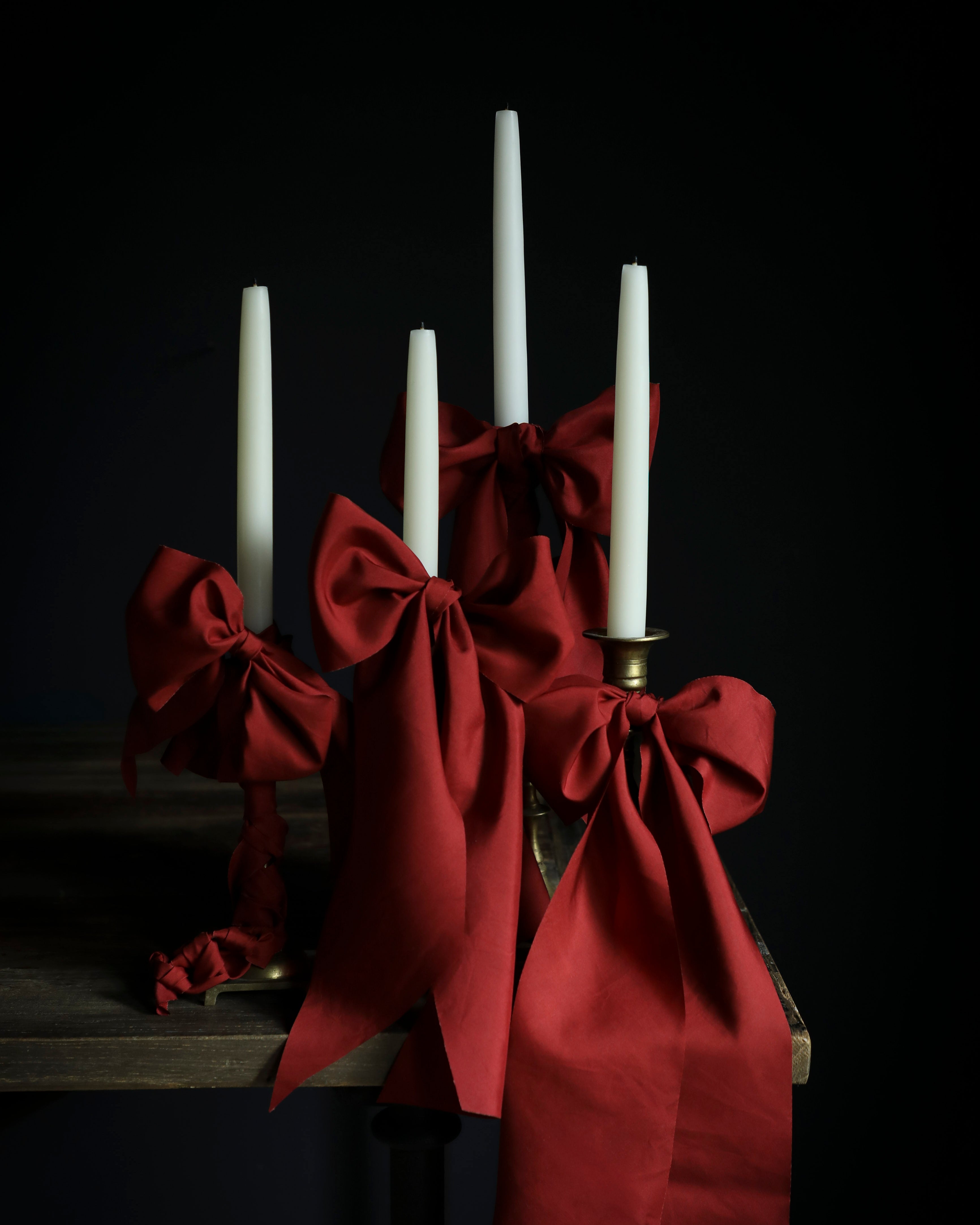 Red taffeta silk ribbon bows with white candles on a dark background