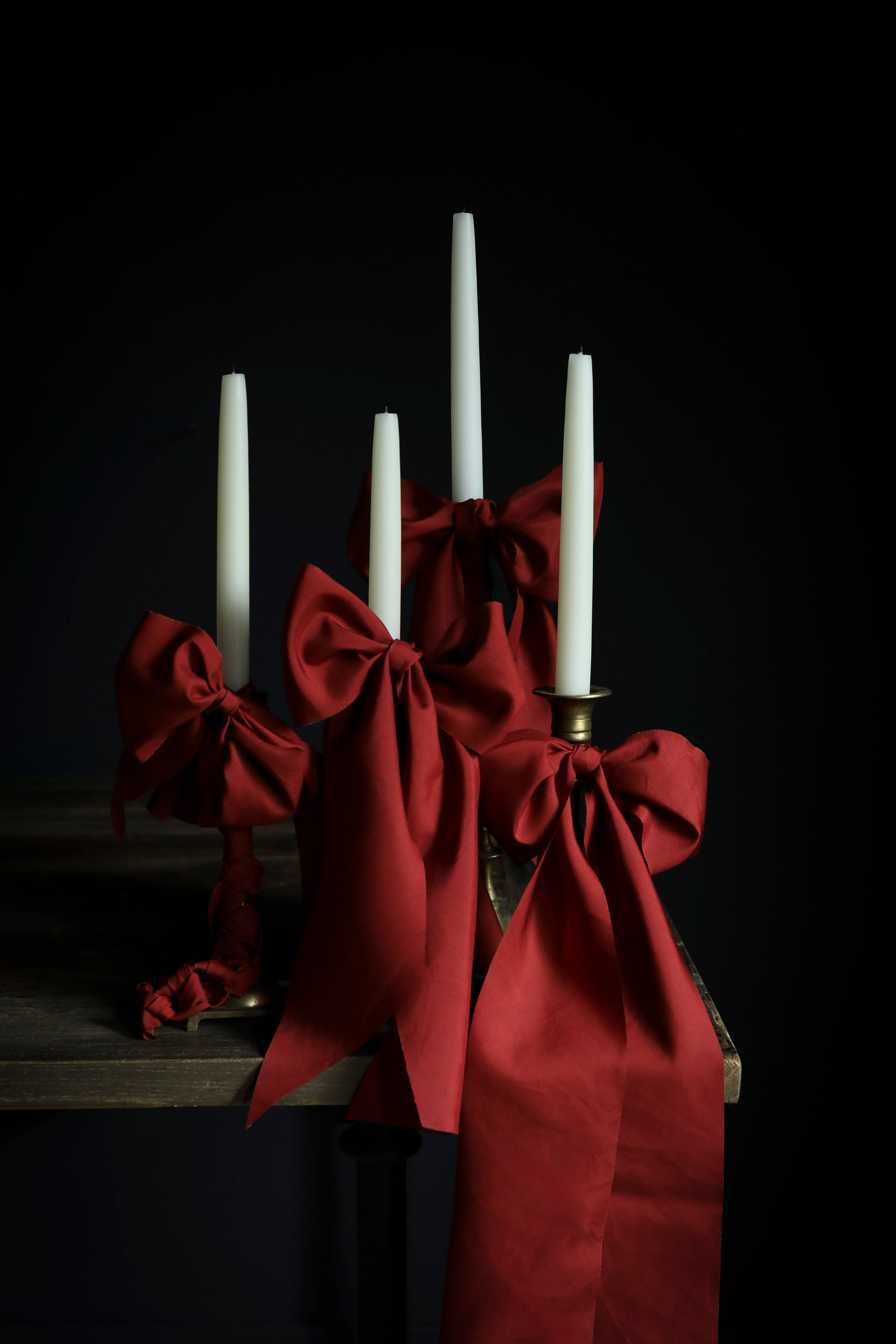 Red taffeta silk ribbon bows with white candles on a dark background