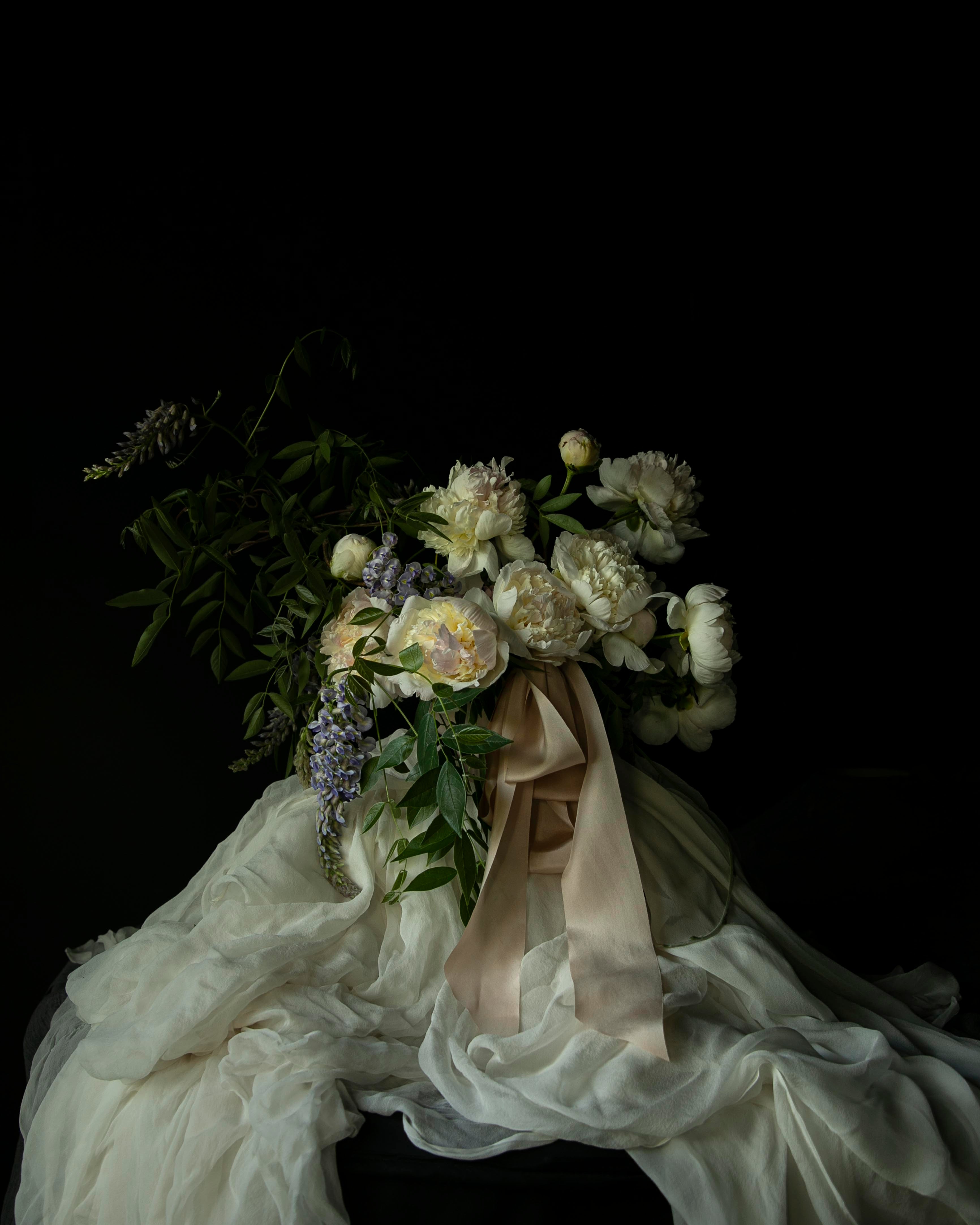Bouquet of peony flowers tied with blush silk ribbon on antique white silk fabric against a black background