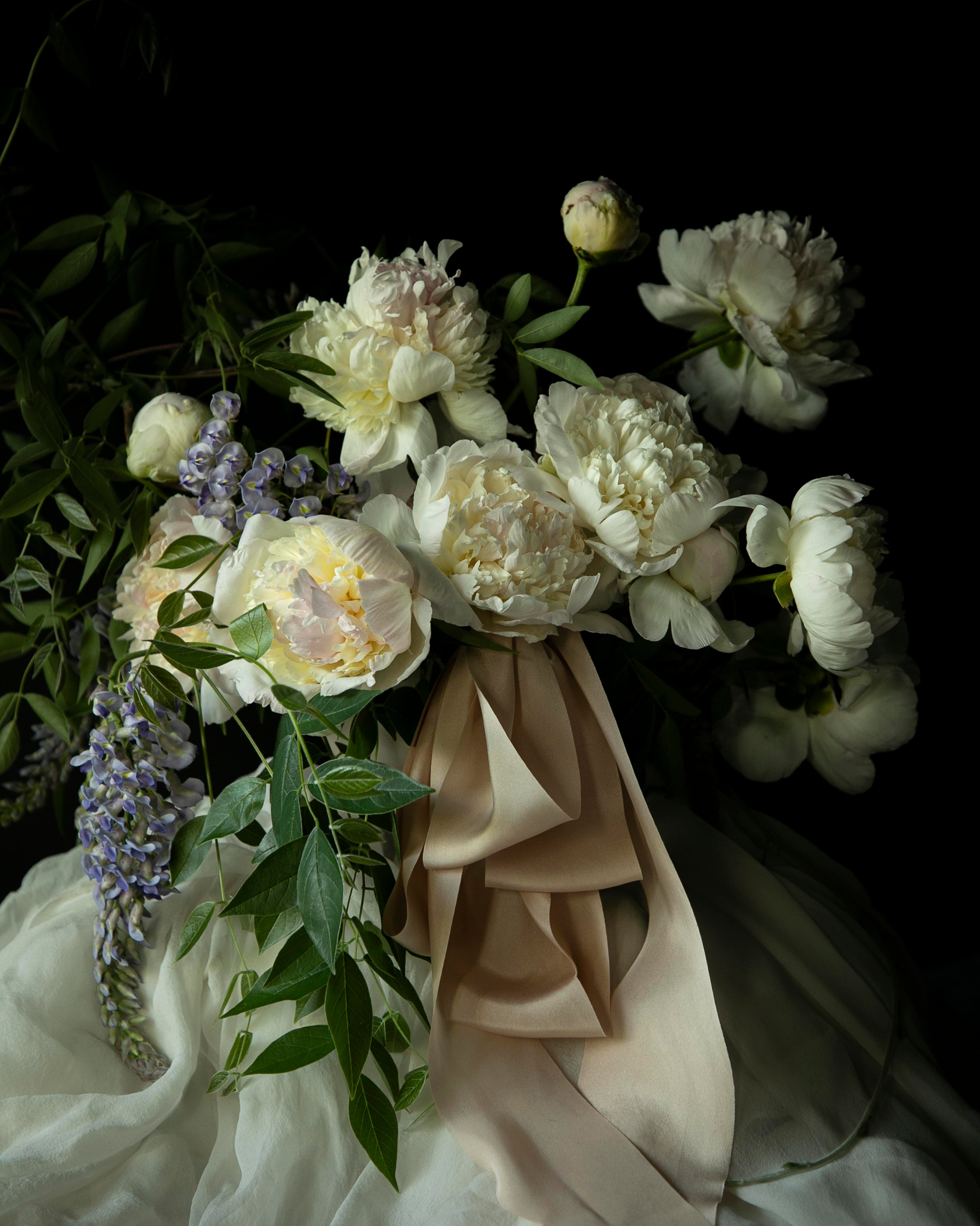 Bouquet of white flowers with greenery and blush silk ribbon against a dark background. dutch master mood for weddings.