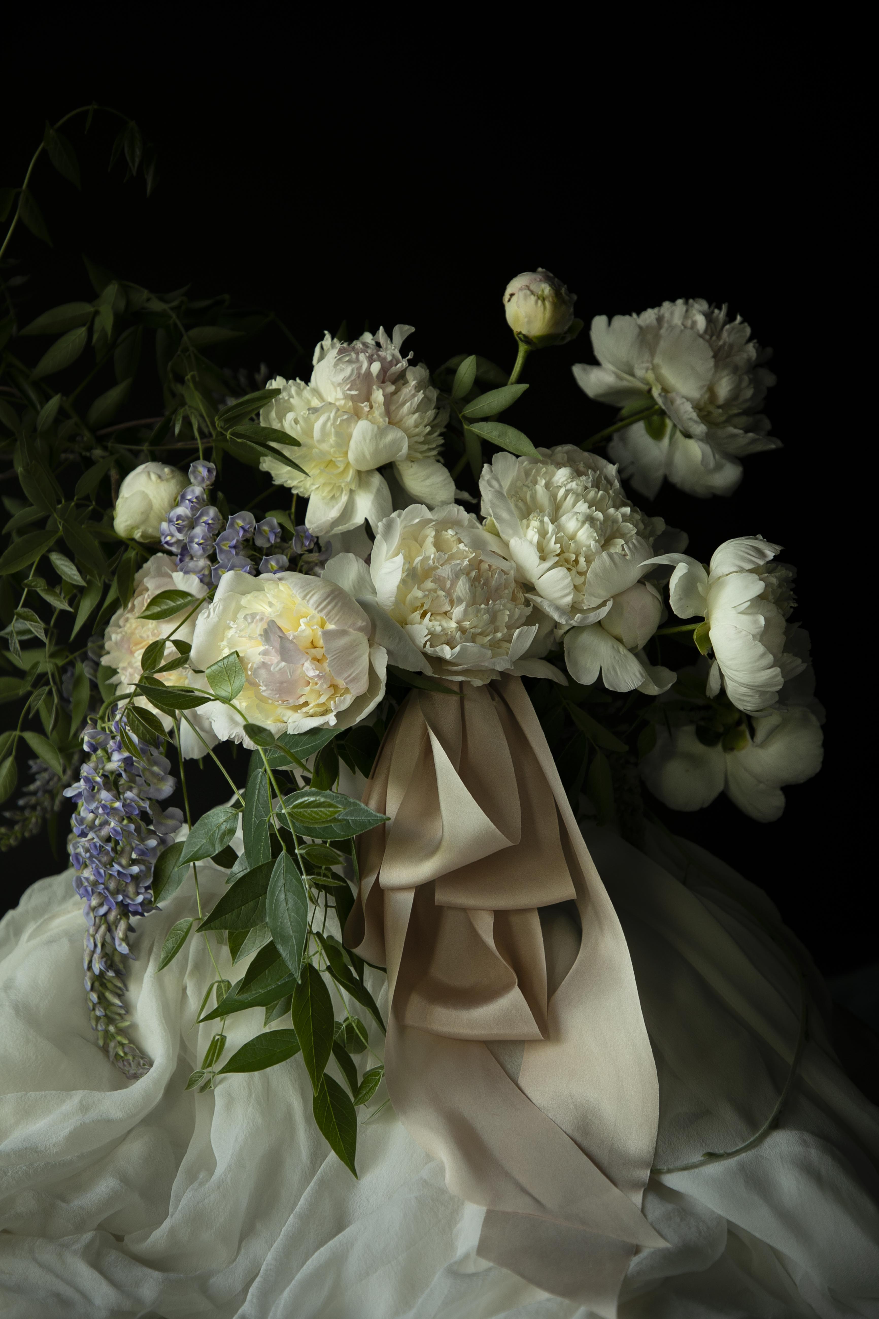 Bouquet of white flowers with greenery and blush silk ribbon against a dark background. dutch master mood for weddings.