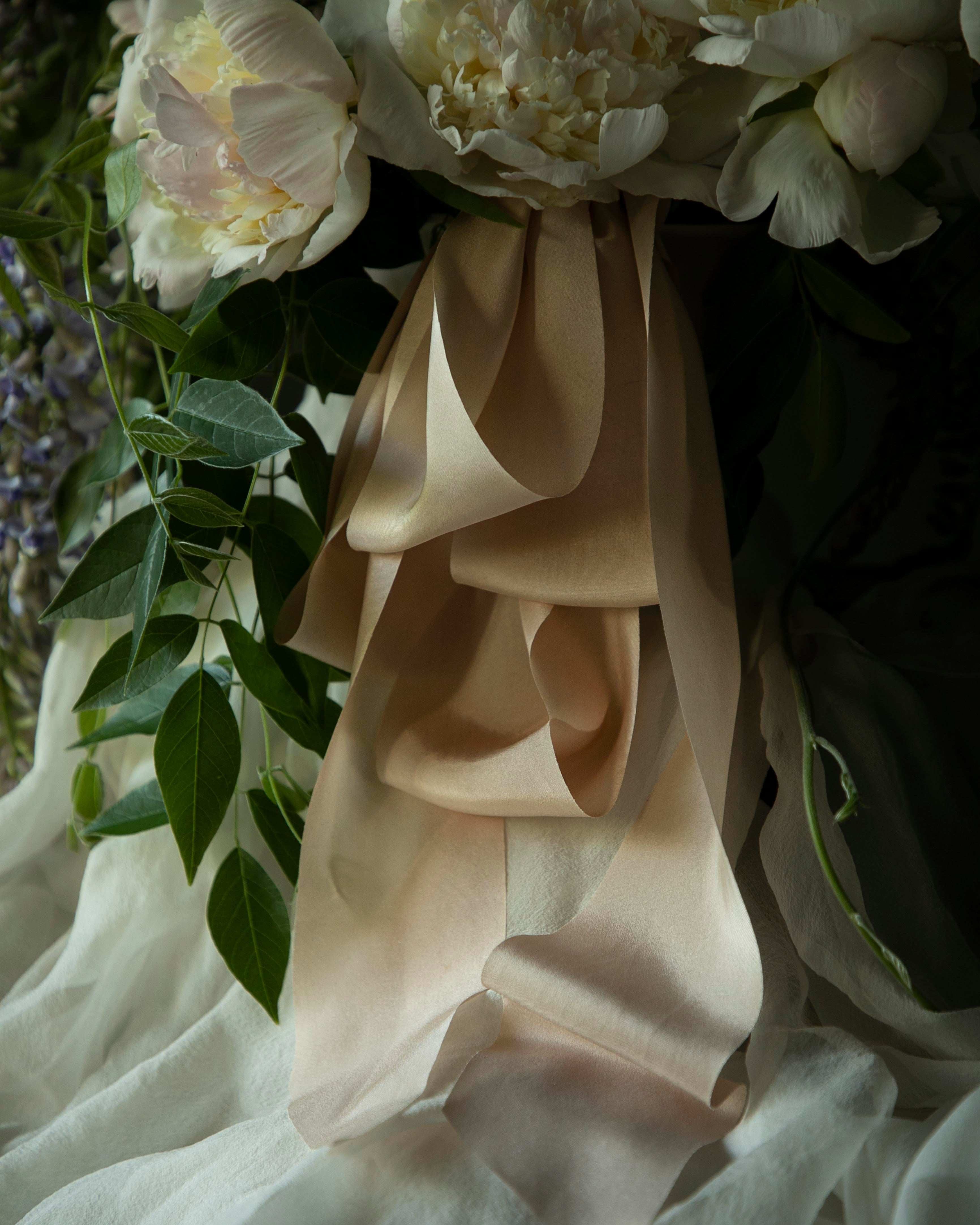 Close-up of a bouquet with white flowers and blush silk ribbons, with a dark, moody background