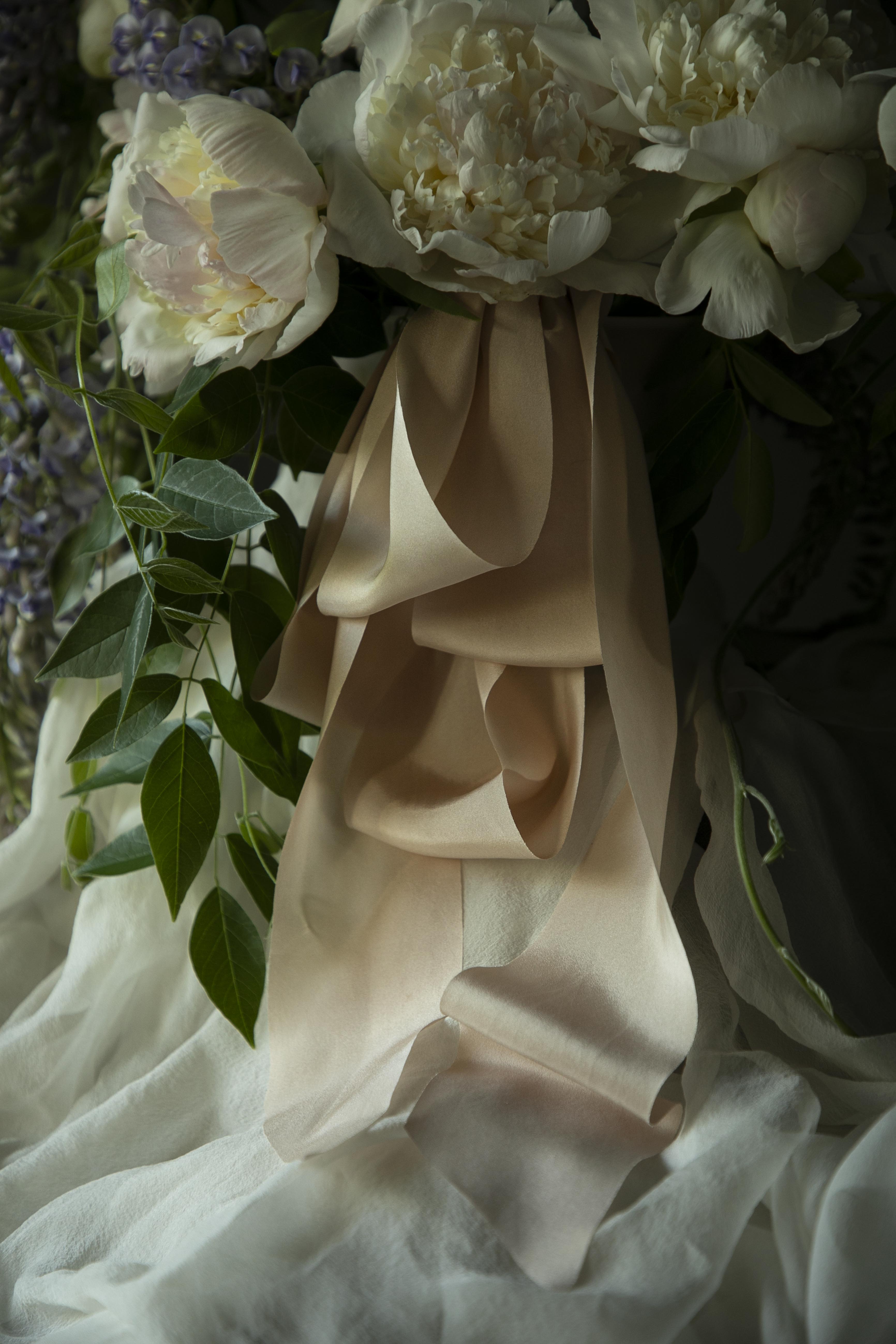 Close-up of a bouquet with white flowers and blush silk ribbons, with a dark, moody background
