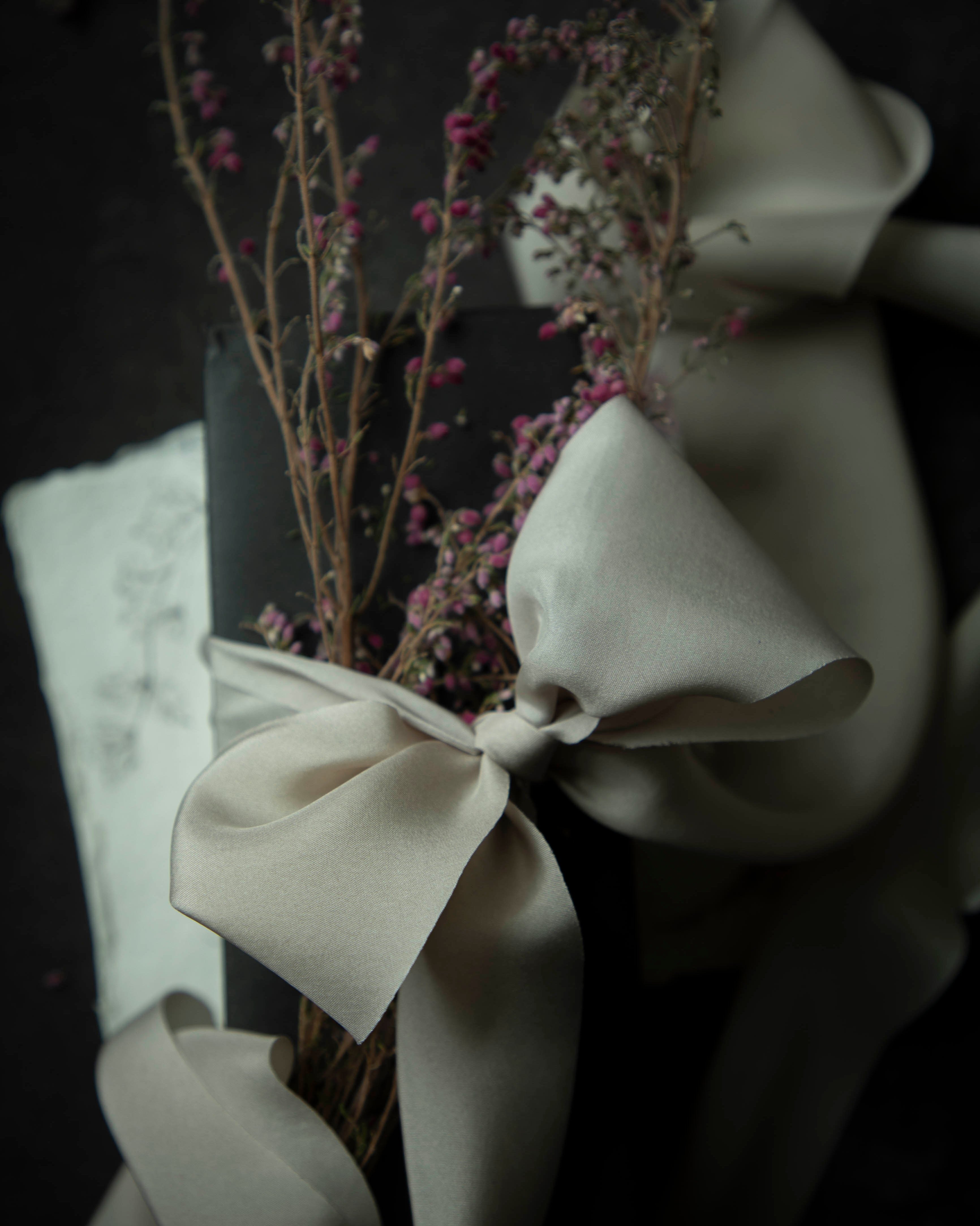 close up of champagne colored ribbon bow tied on a black box against a black background
