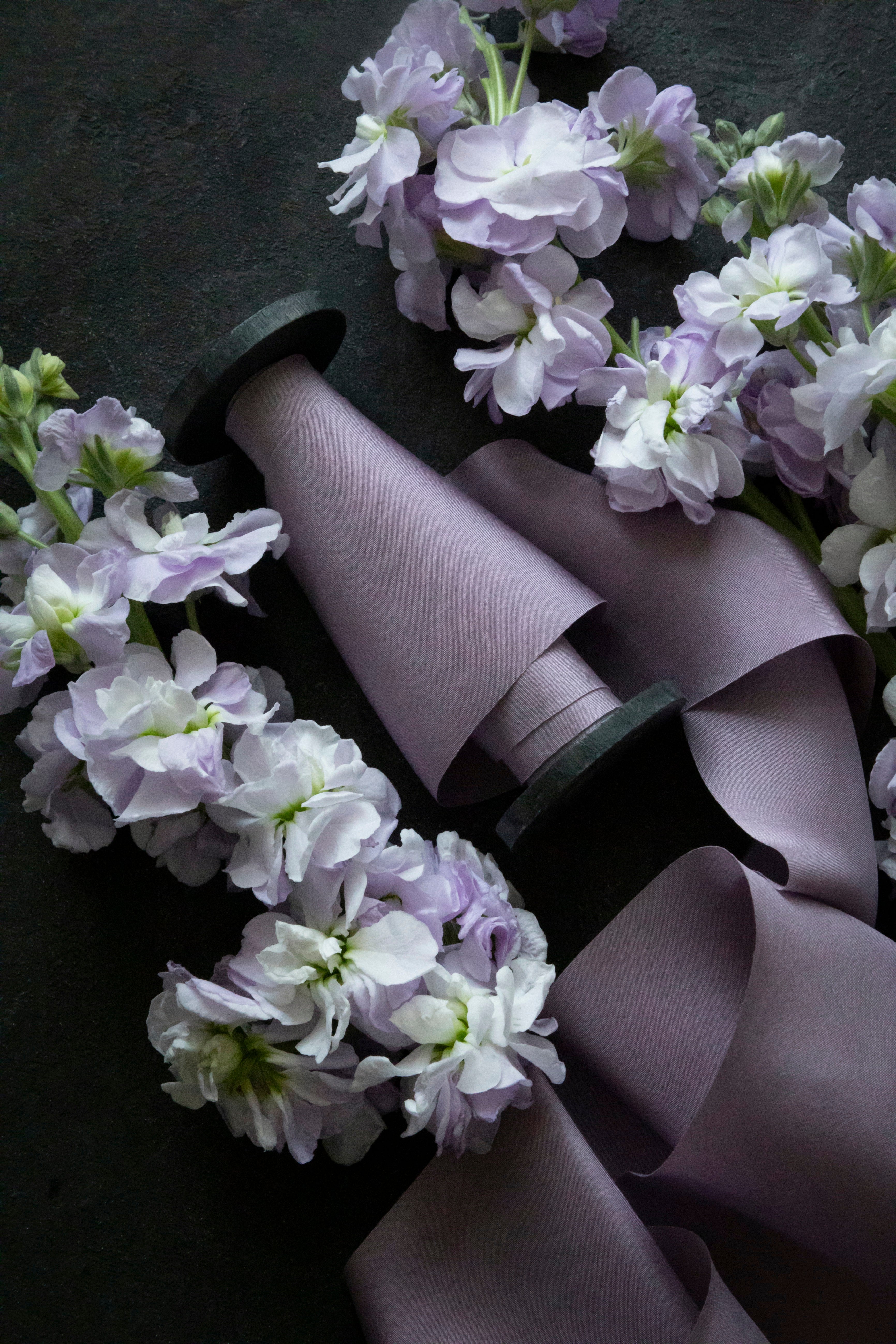lilac colored silk ribbon on wooden spool surrounded by purple stock flowers