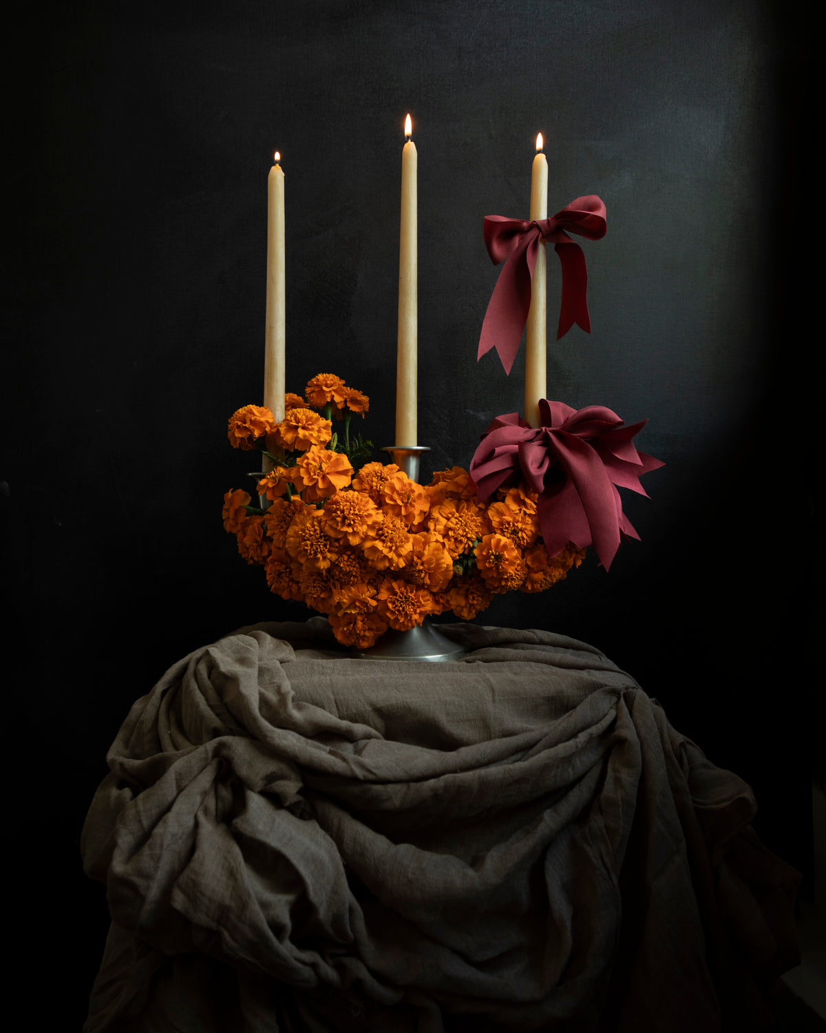 artful floral display with marigold flowers and red ribbon bows stacked on candles. Creative floral centerpiece