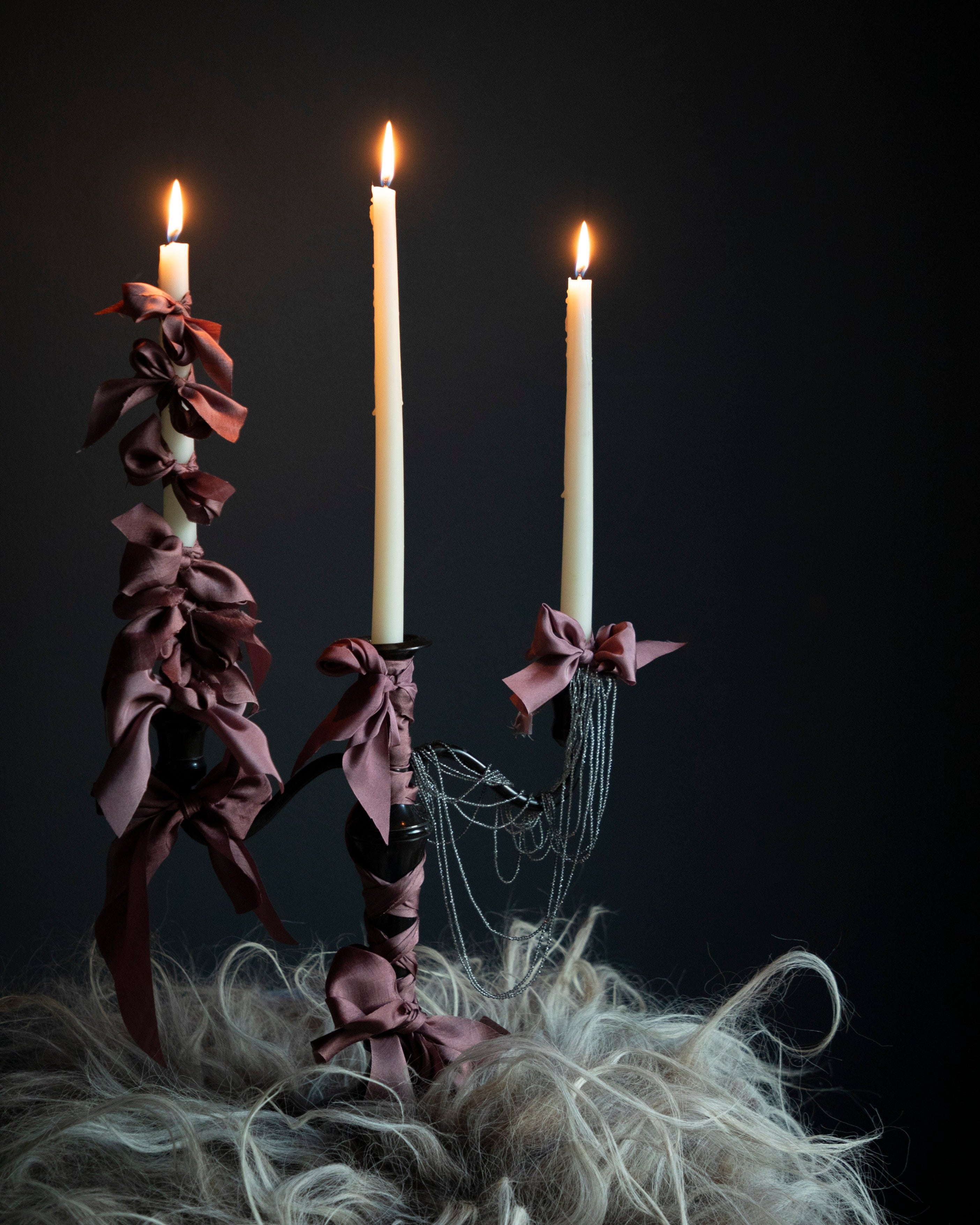 candle holder witth silk ribbon bows against a dark background. moody viking feel.