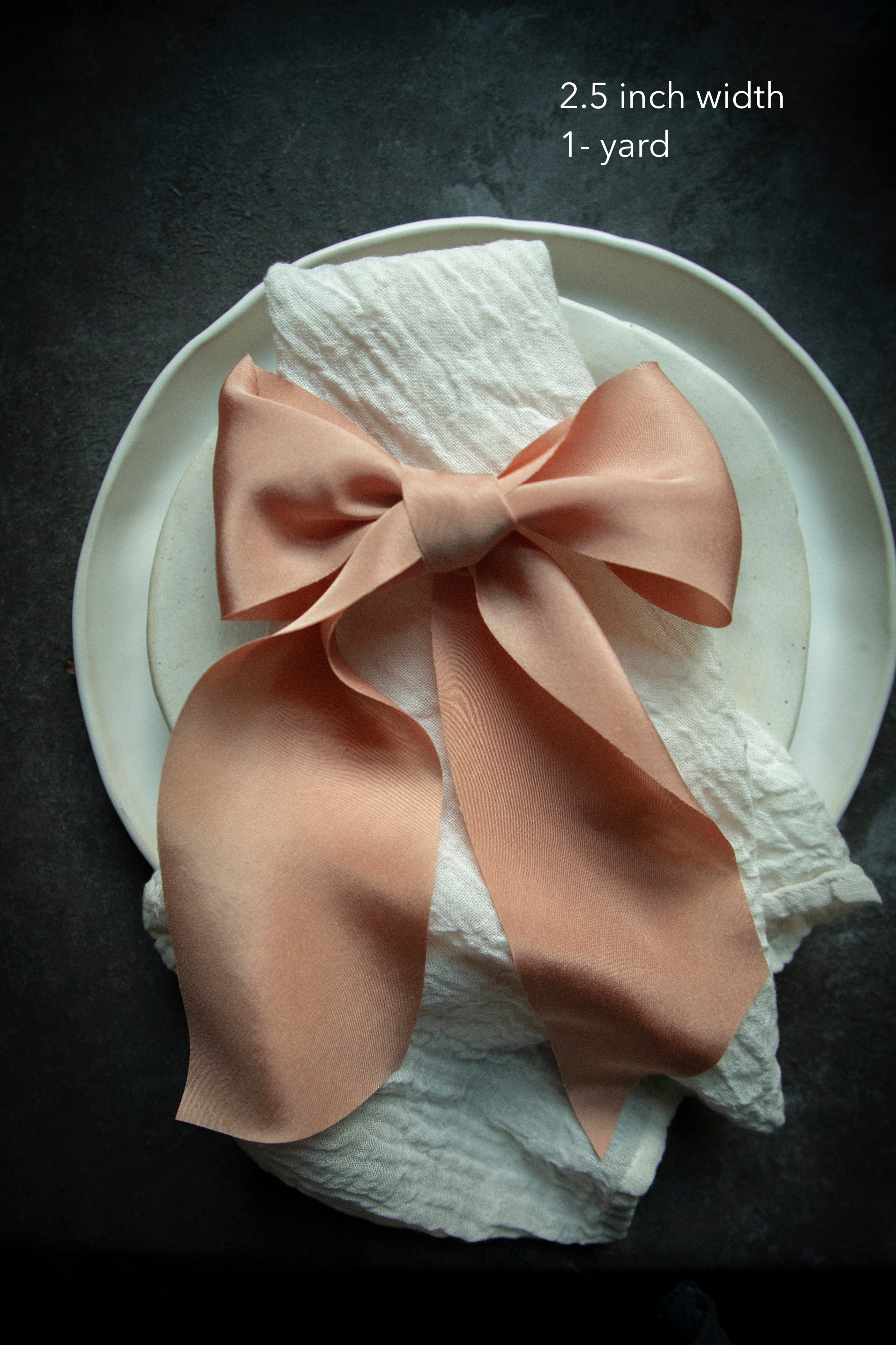 An elegant soft coral organic loomed silk ribbon tied into a bow on a cotton napkin, highlighting intricate details for creating the perfect ribbon bow. Ideal for wedding accents such as bridal bouquets, invitation wraps, and table decor.