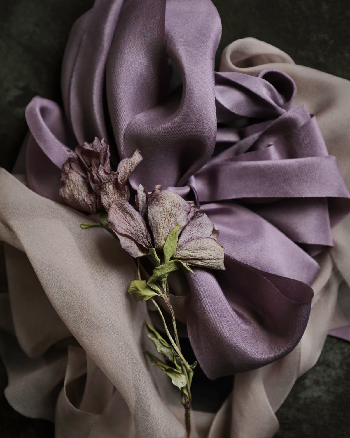 pile of purple and mauve silk ribbons with a dried flower with matching colors.