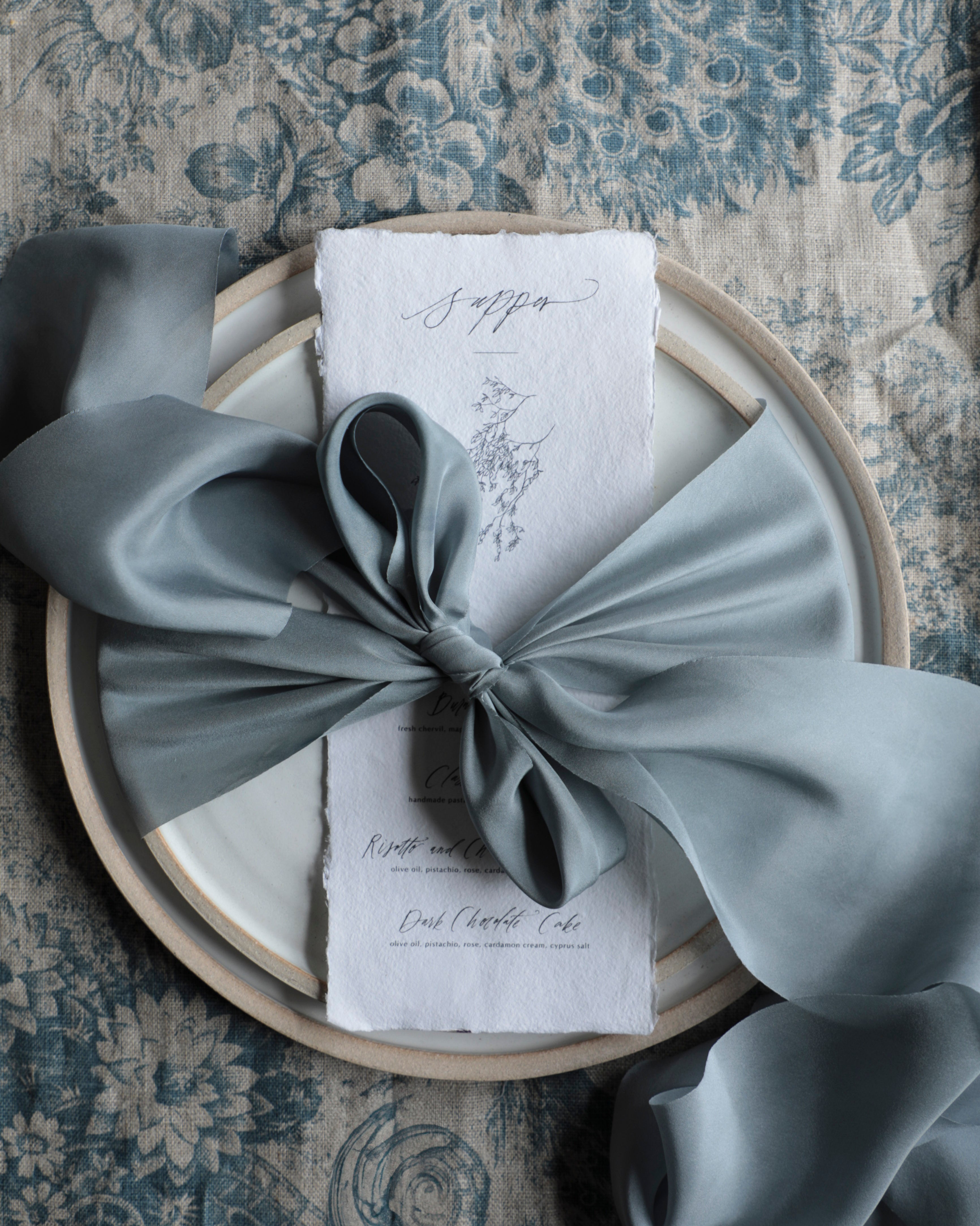 blue bow on a white napkin with text, placed on a textured surface.