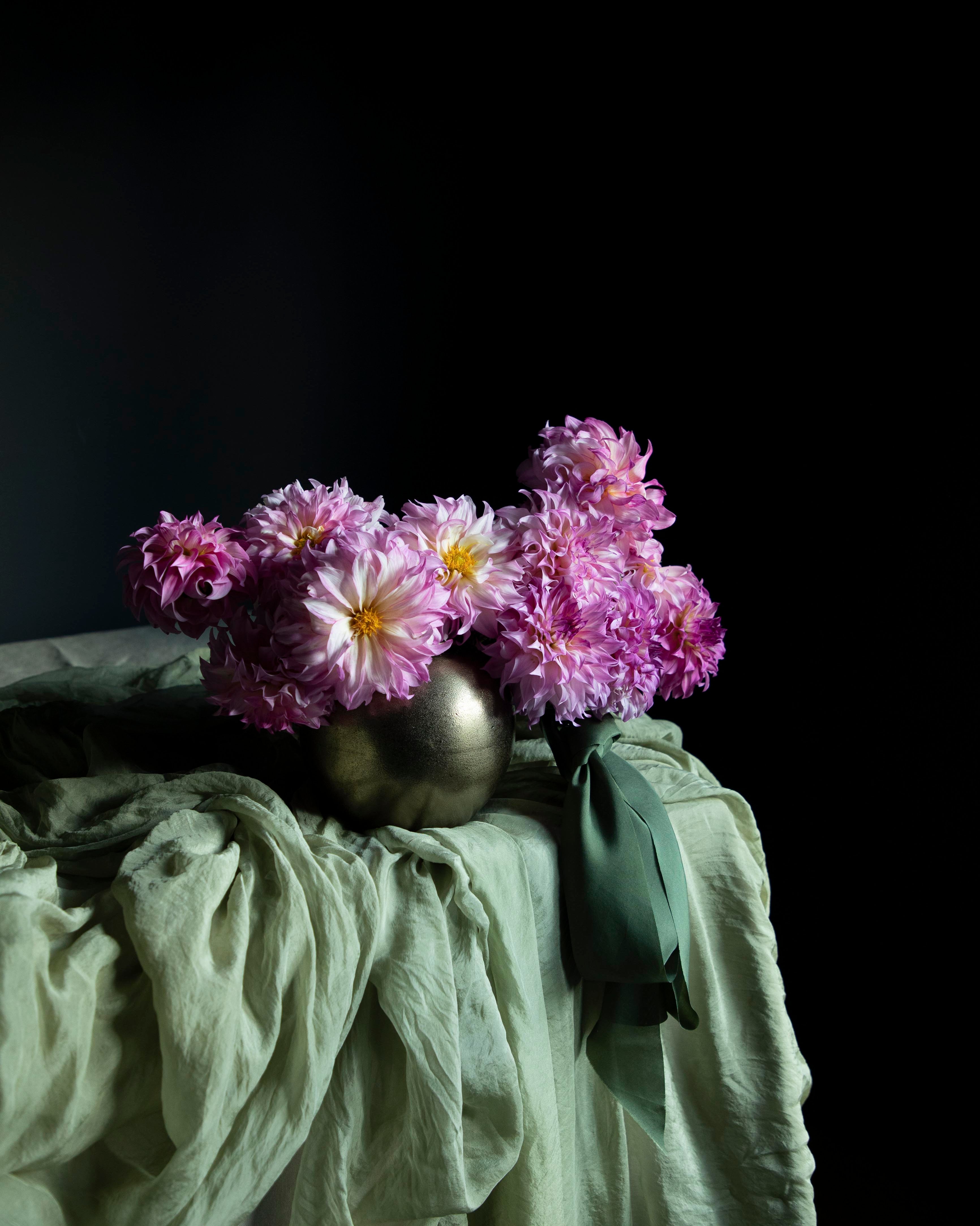 Vase with purple flowers on a draped surface against a black background