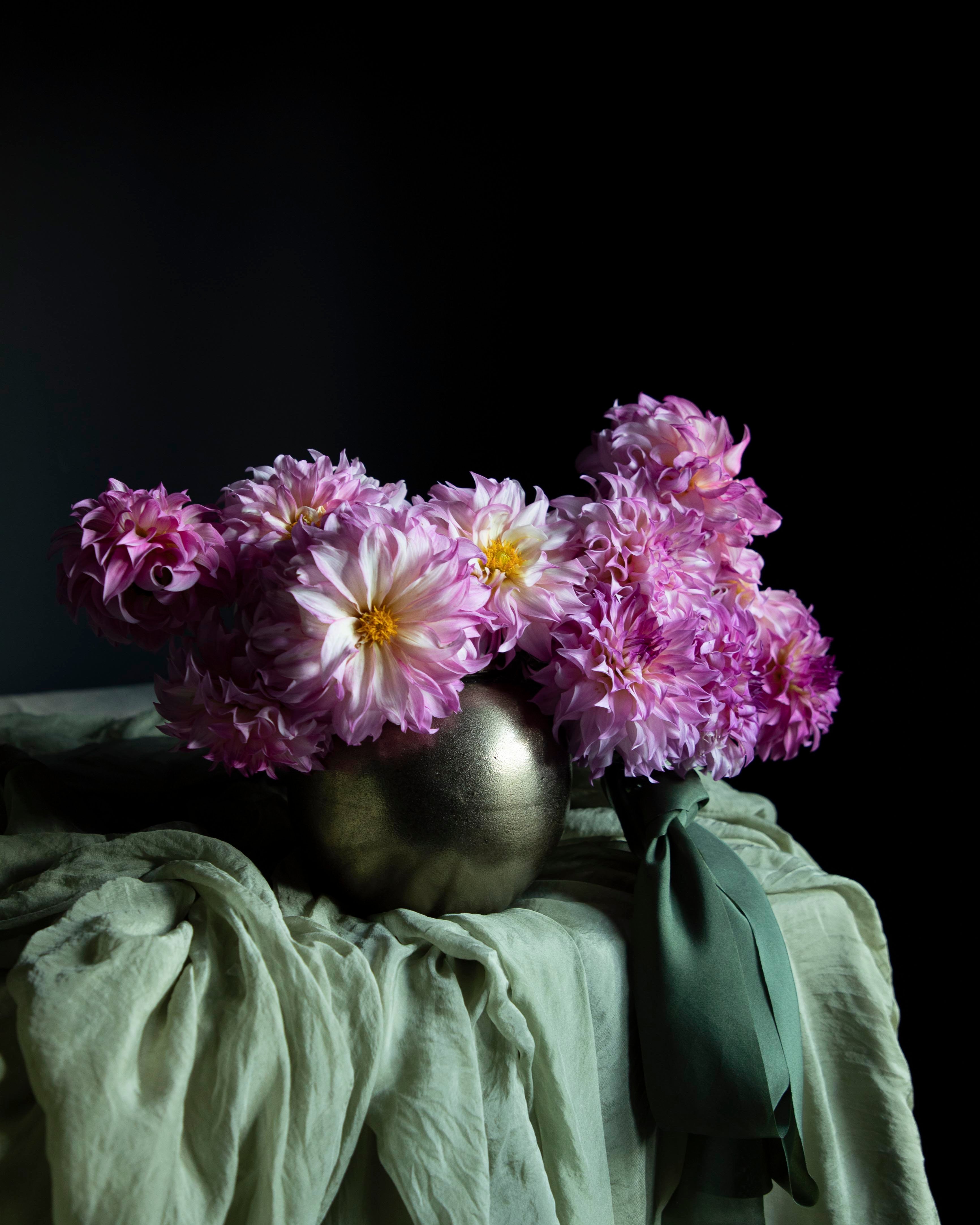 Pink flowers in a metallic vase on a green cloth with a dark background