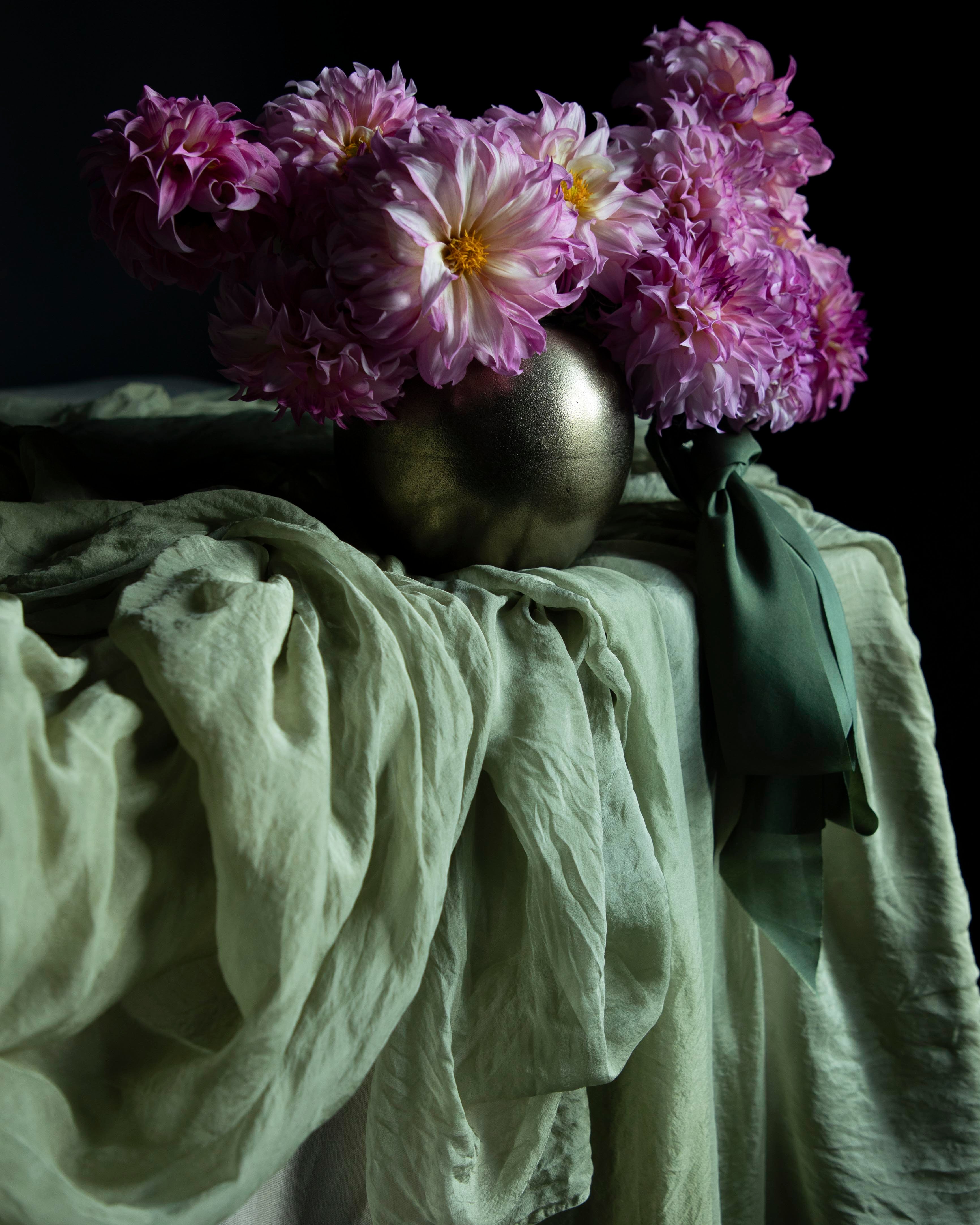 Purple flowers in a metallic vase on a draped silk fabric surface with a dark background