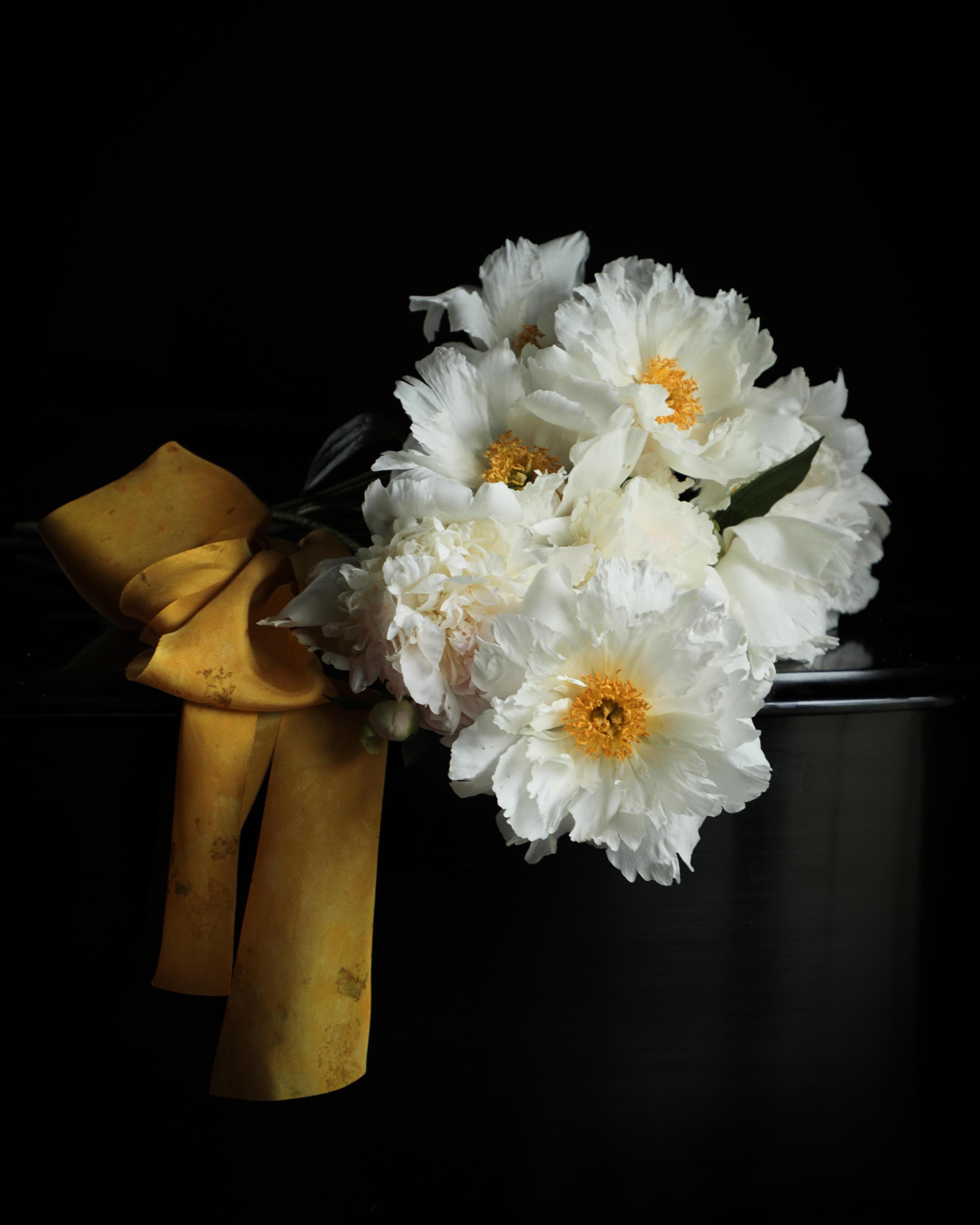 White peony flowers with yellow centers and a gold ribbon bow on a black background