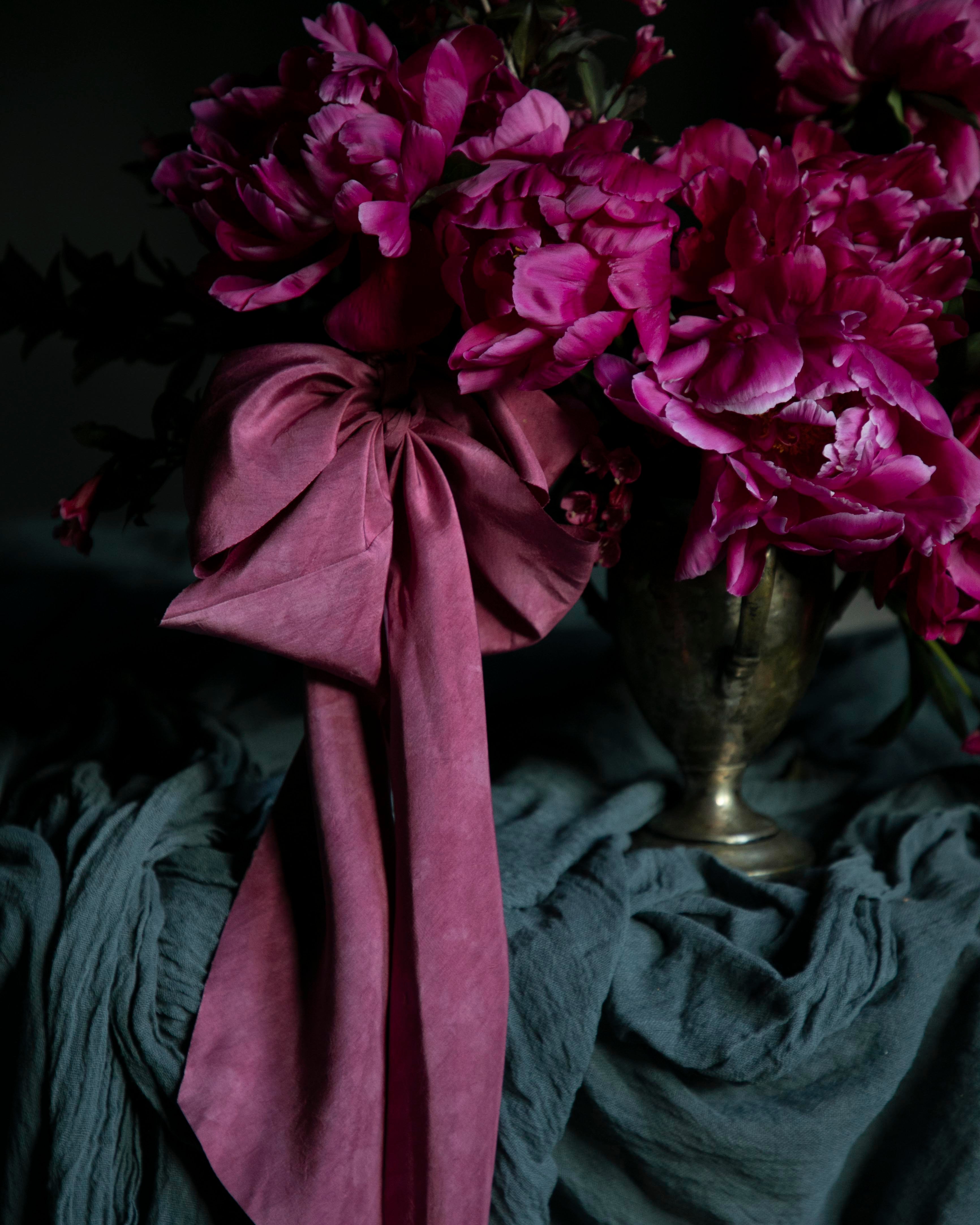 Pink flowers with a large pink bow in a silver vase on a dark background. opalite aesthetic.
