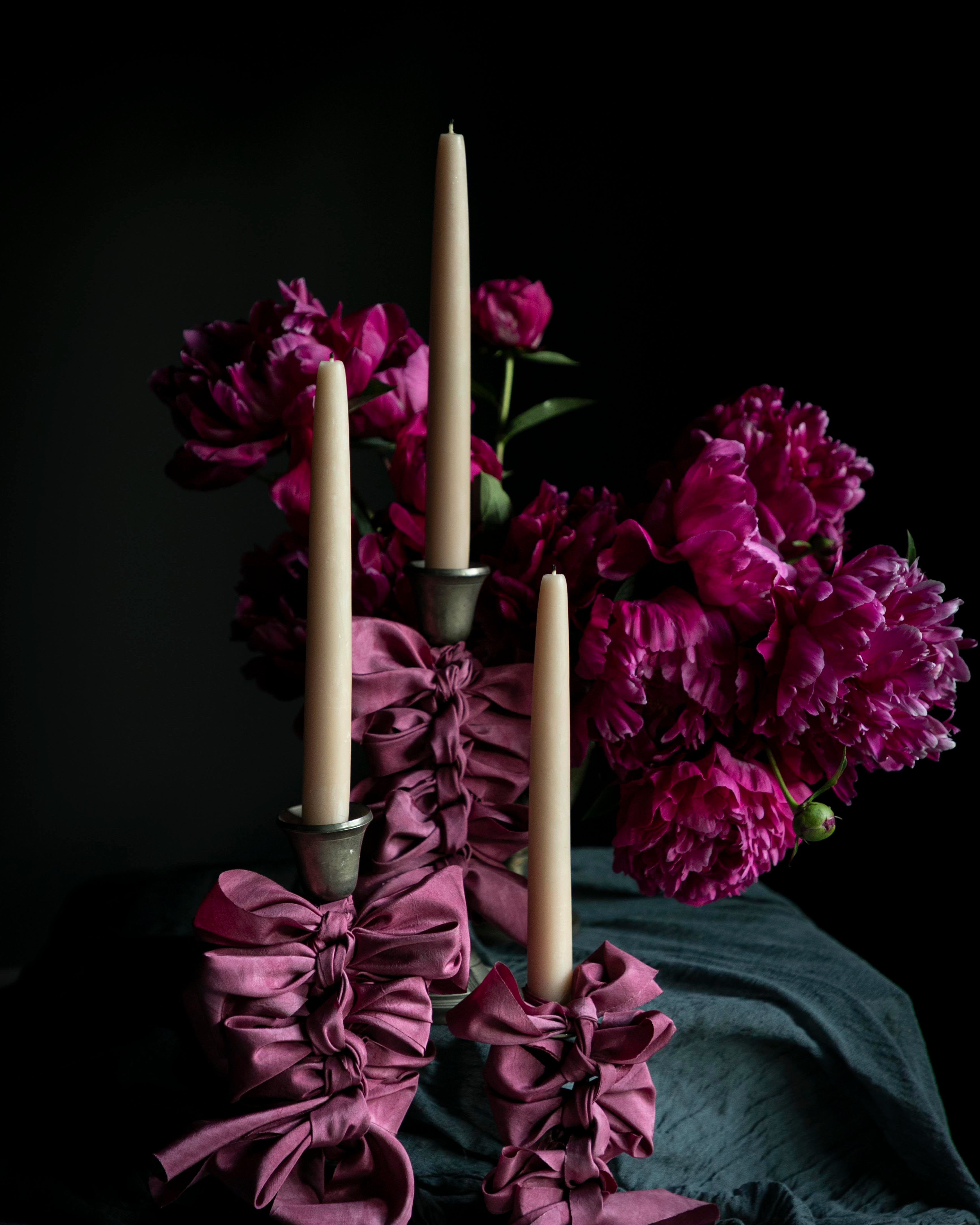 Candle holder with purple ribbons and candles in front of pink flowers on a dark background