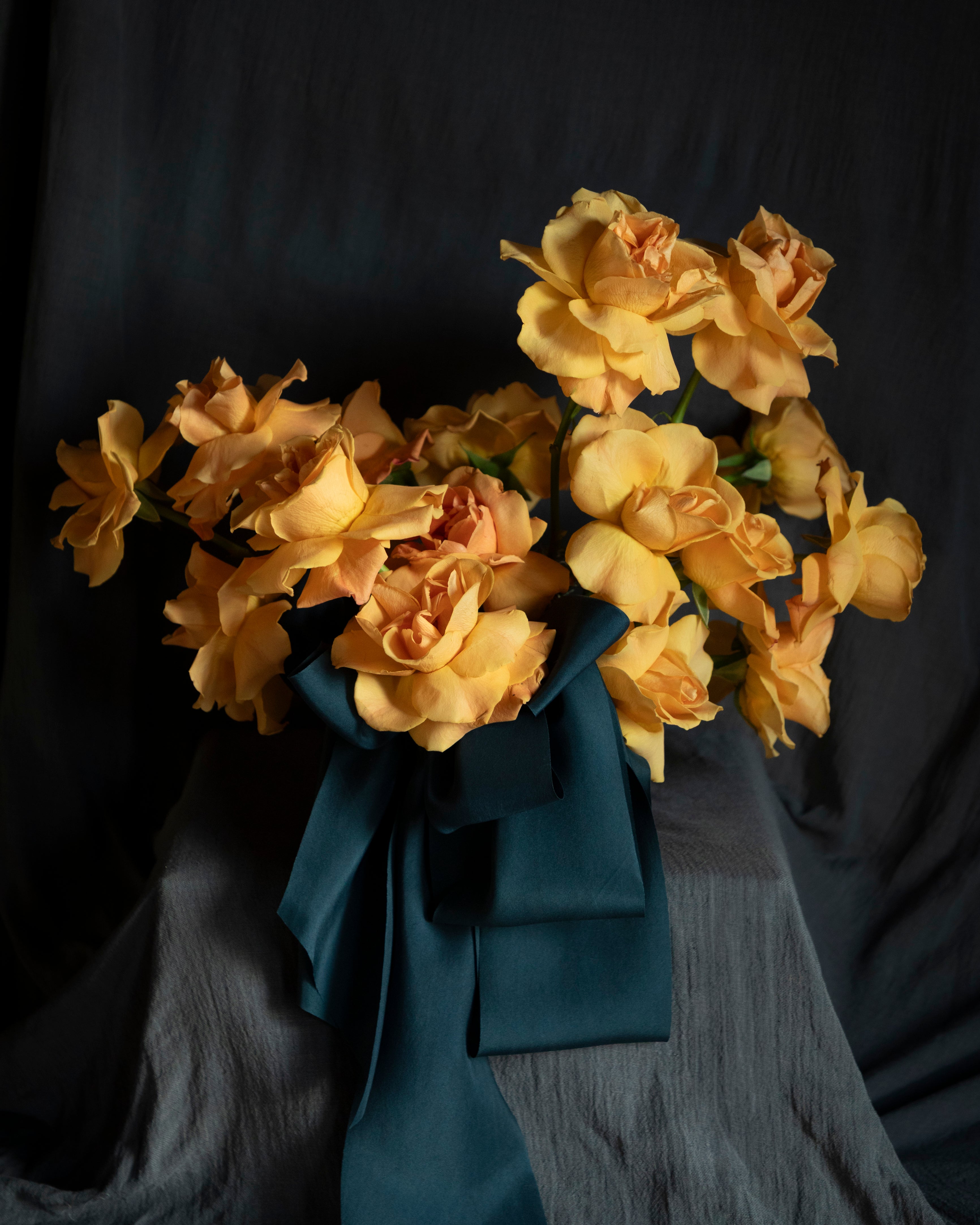 Bouquet of orange-yellow flowers with a blue ribbon on a dark background