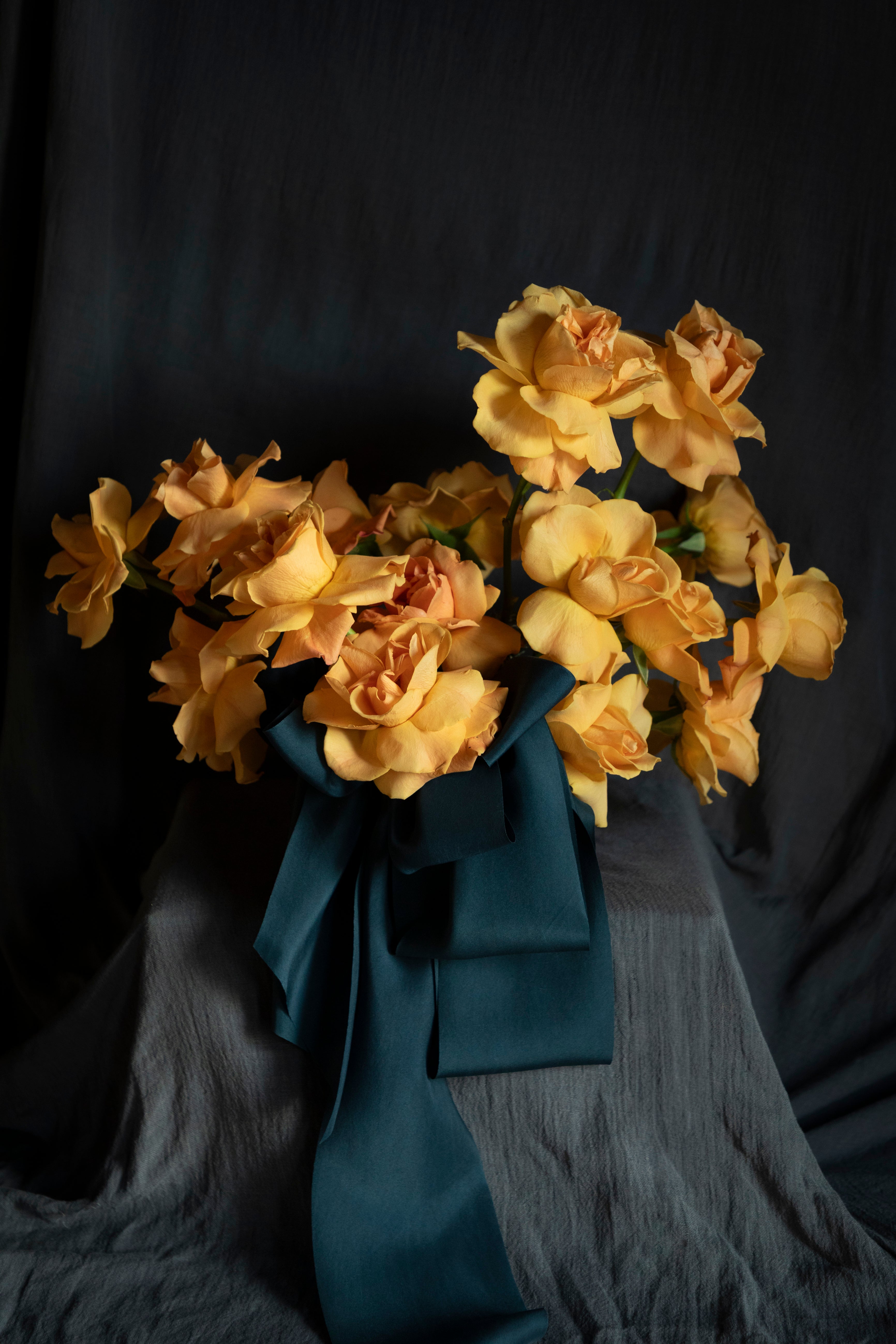 Bouquet of orange-yellow flowers with a blue ribbon on a dark background