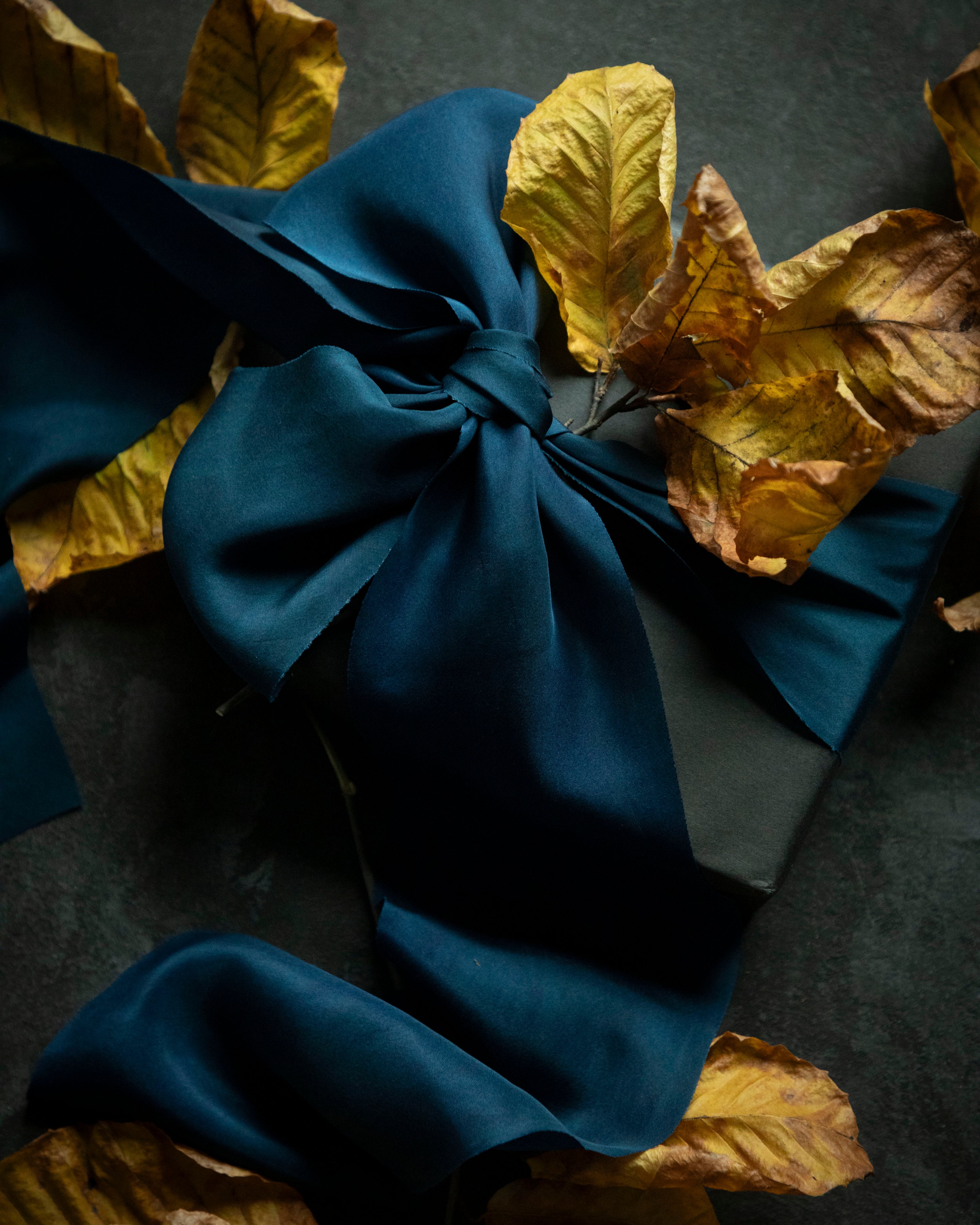 black gift box wrapped with a large bow on a dark surface with yellow leaves