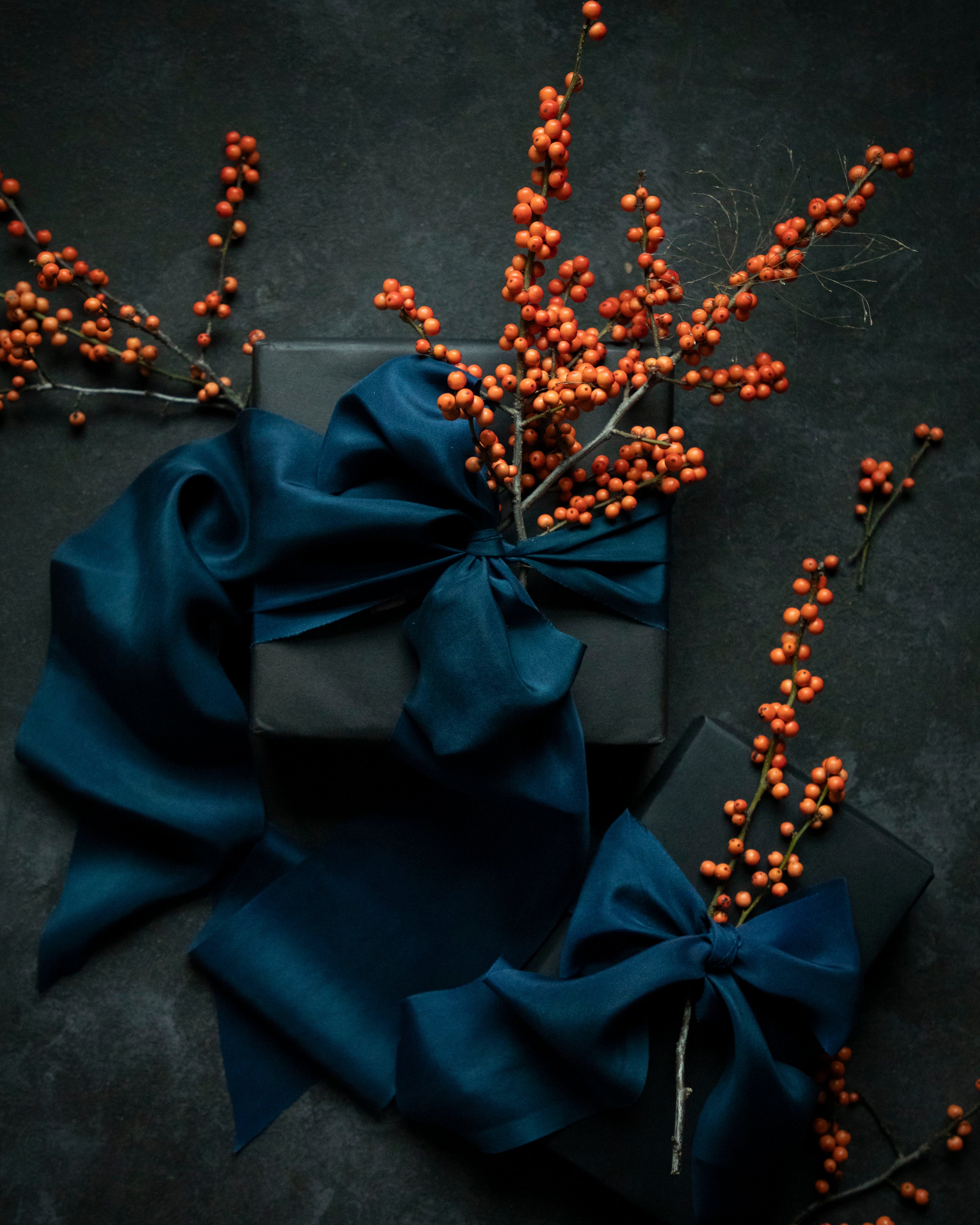 Dark gray gift box with blue ribbons and orange berries on a dark background