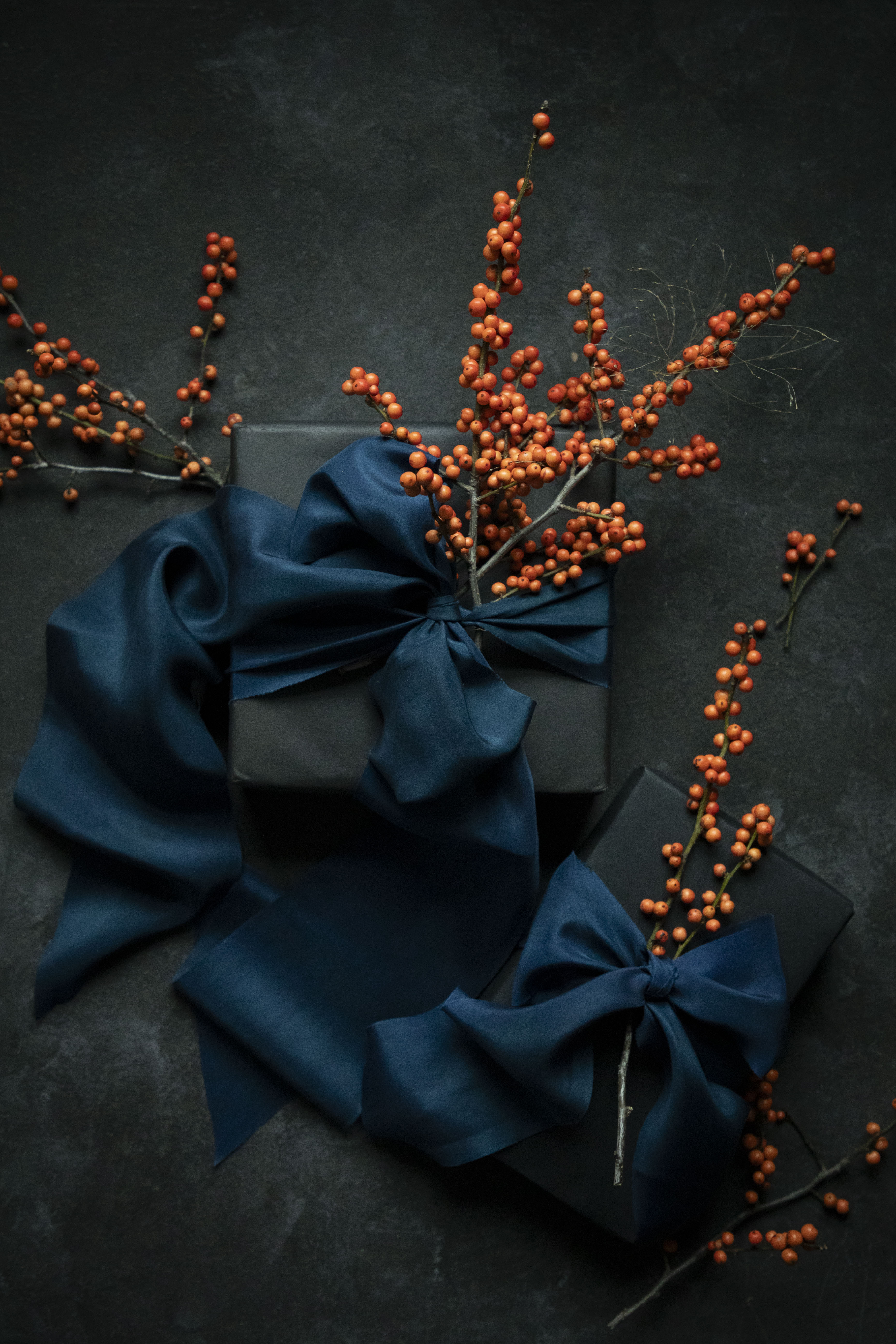 Dark gray gift box with blue ribbons and orange berries on a dark background
