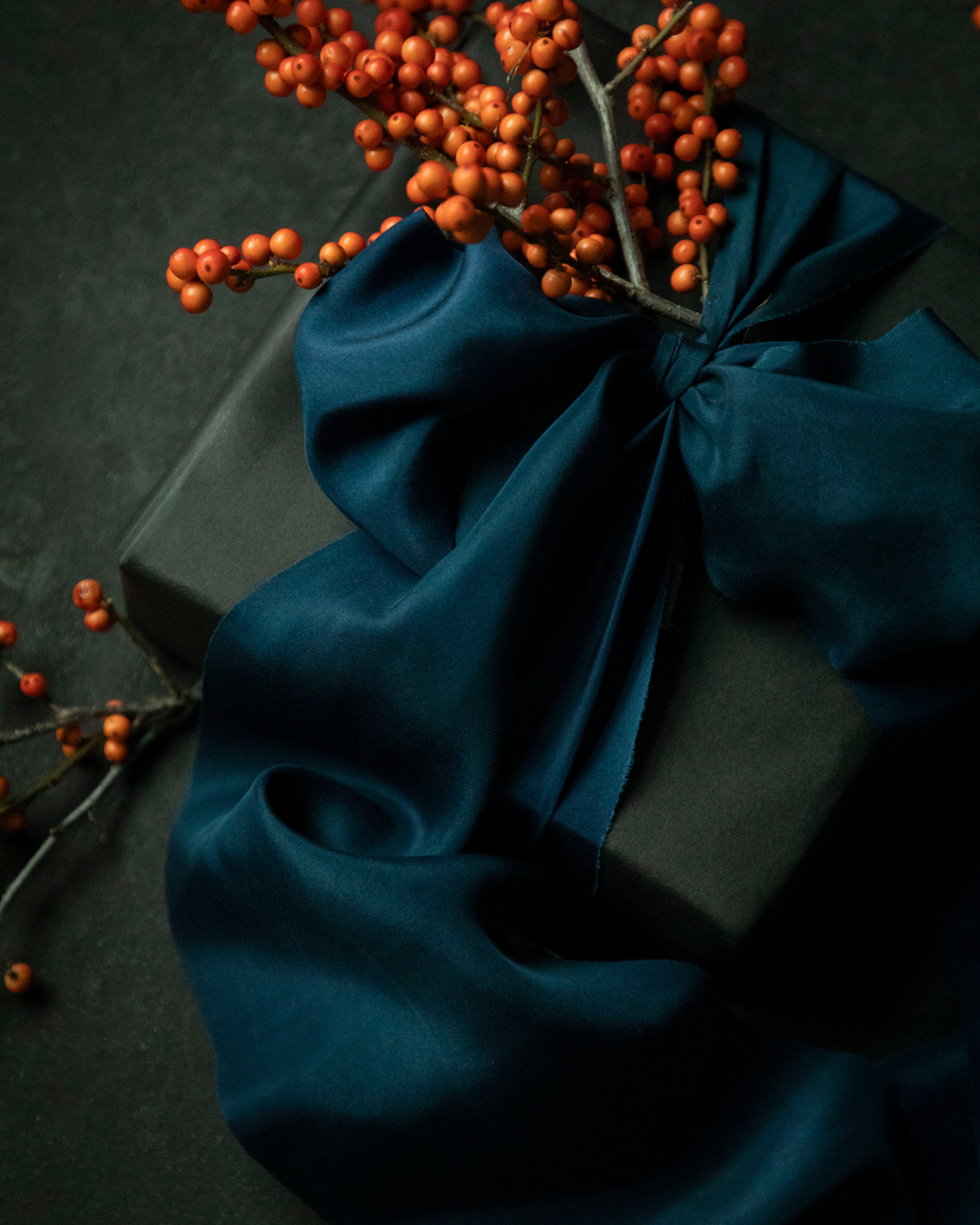 gift wrapping inspiration with a sapphire blue silk ribbon bow and orange berries on a dark background