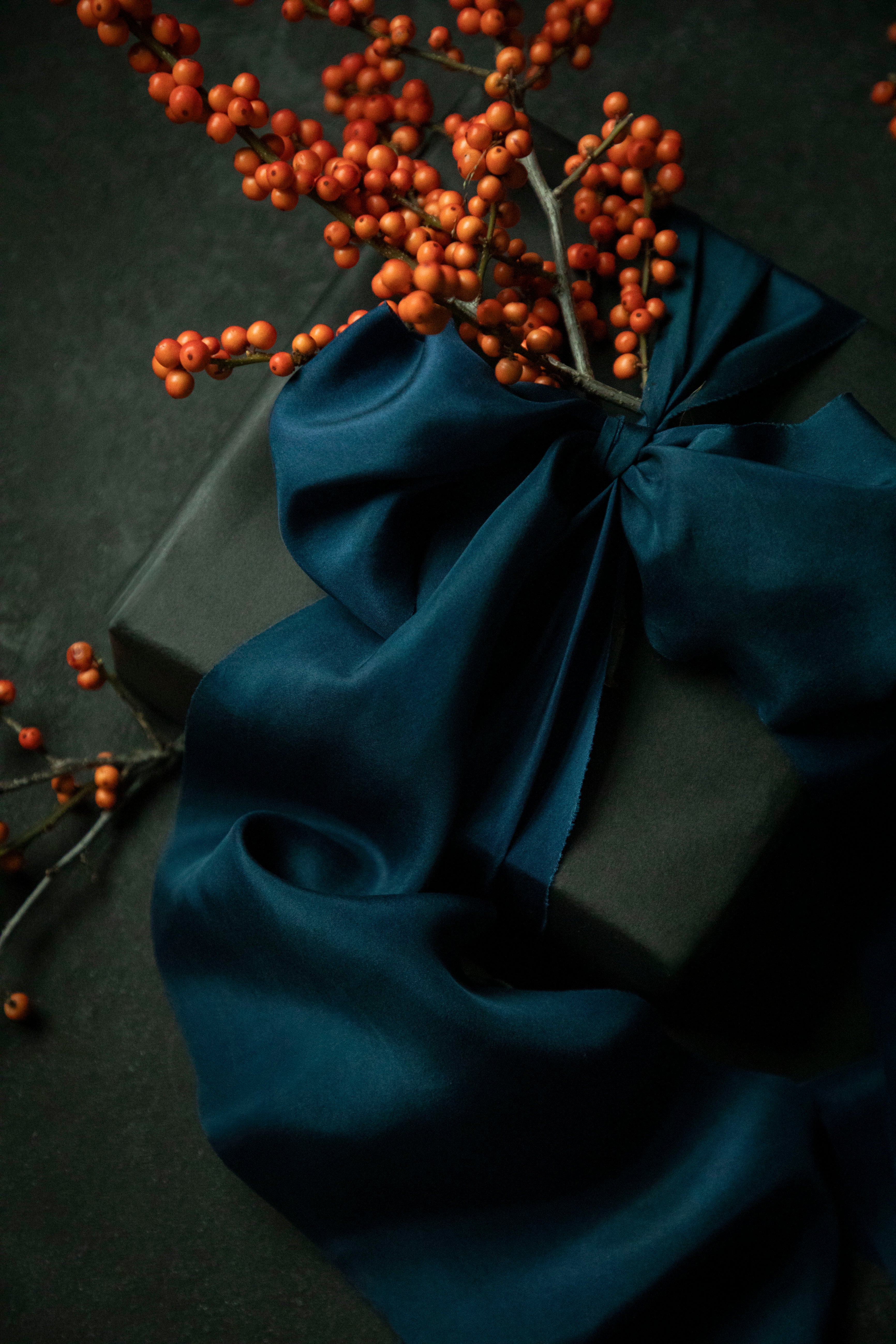 gift wrapping inspiration with a sapphire blue silk ribbon bow and orange berries on a dark background