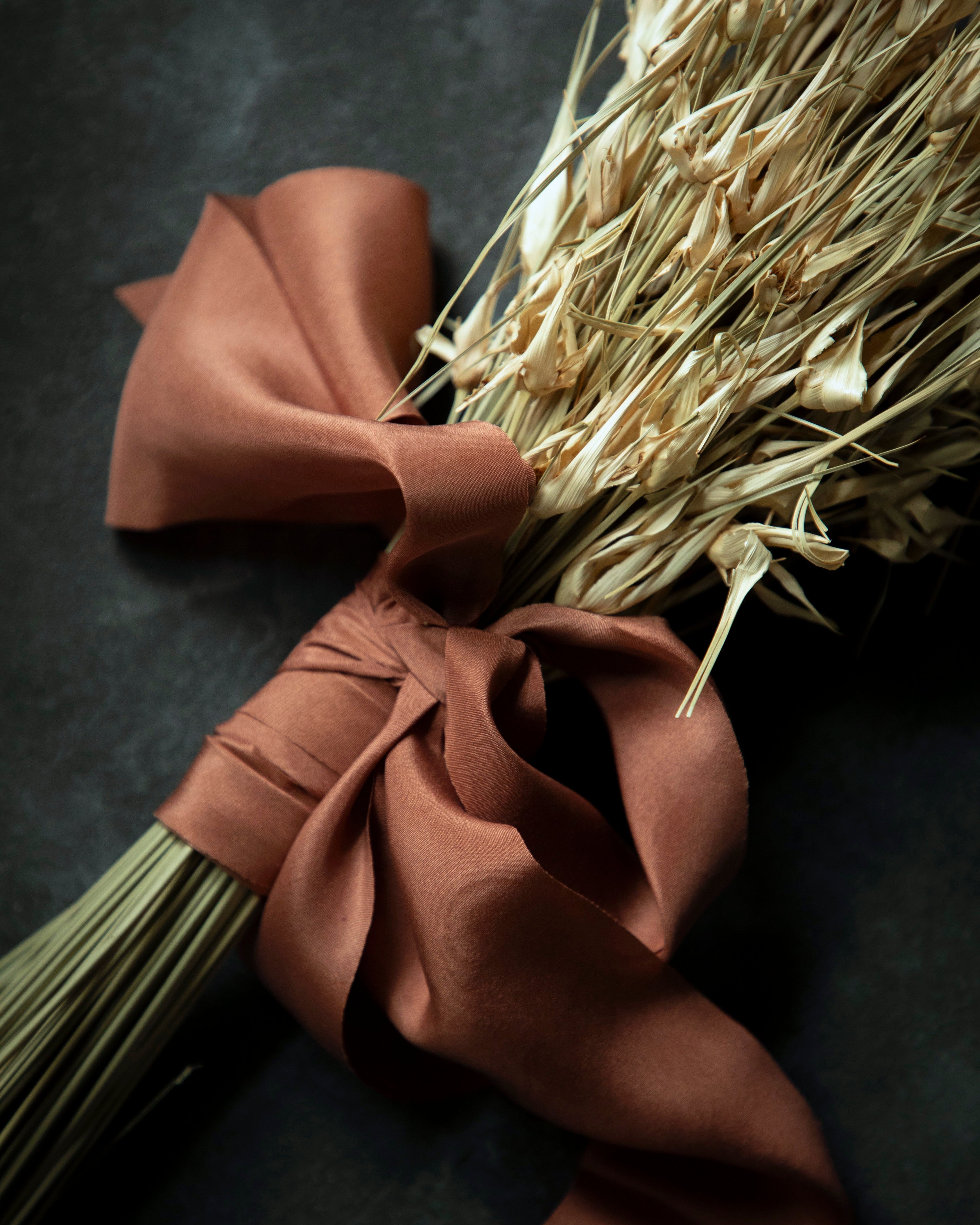 Bouquet of dried grasses tied with a copper silk ribbon on a dark surface