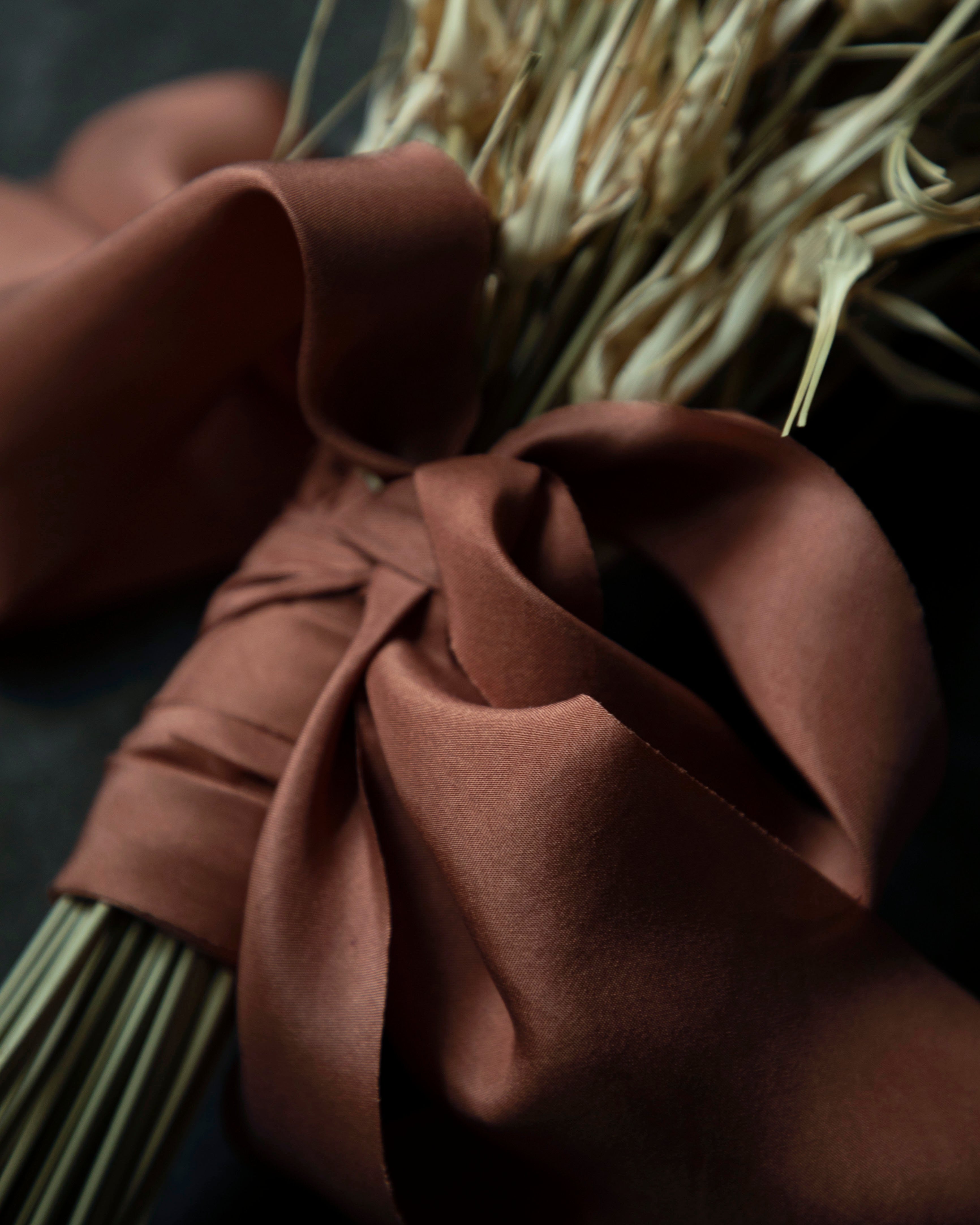 Copper colored silk ribbon around a bundle of dried plants on a dark background