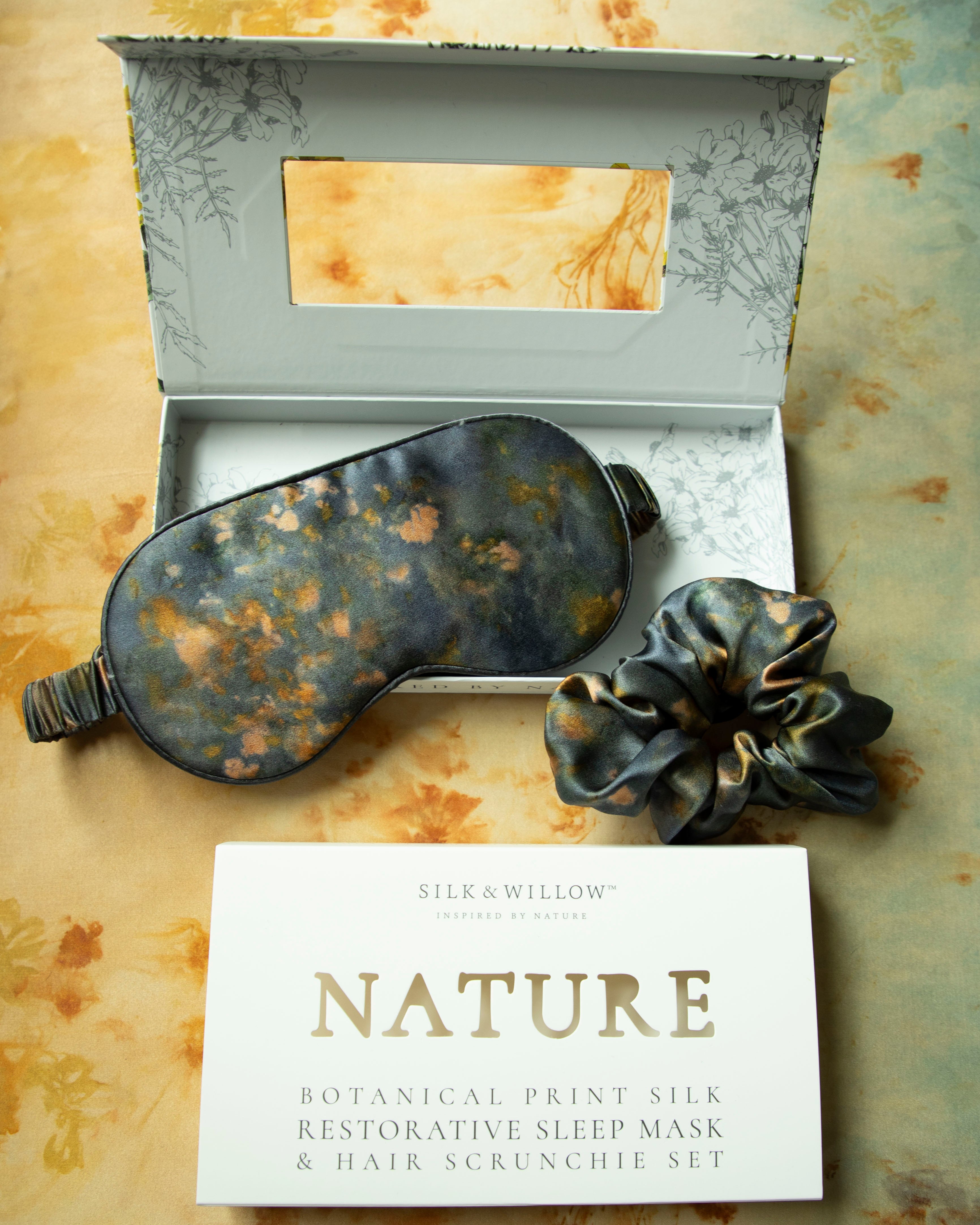 Silk Willows botanical print silk restorative sleep mask and hair scrunchie set on a textured surface.