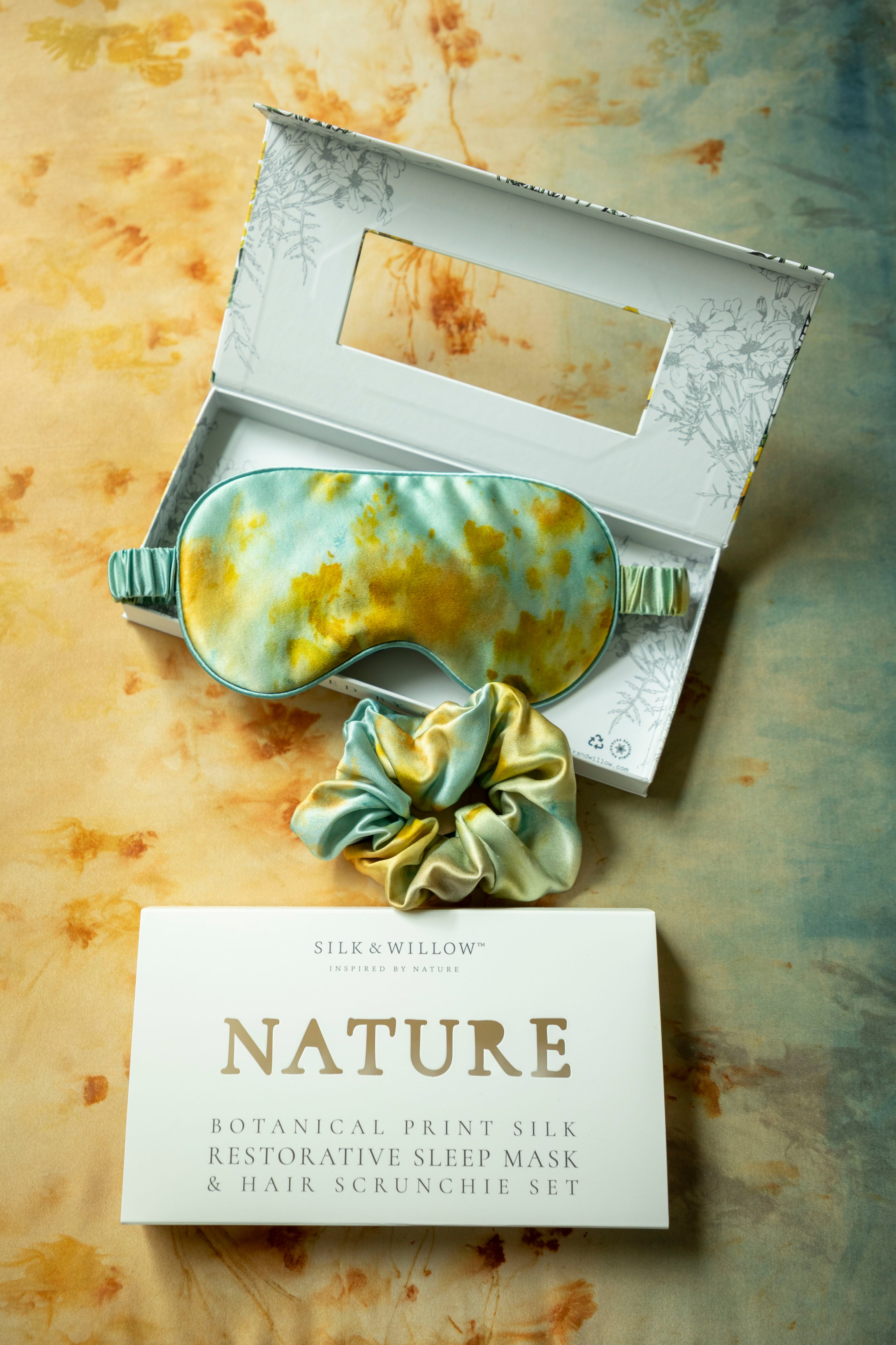 Silk & Willow Nature botanical print silk restorative sleep mask and hair scrunchie set on a textured surface.