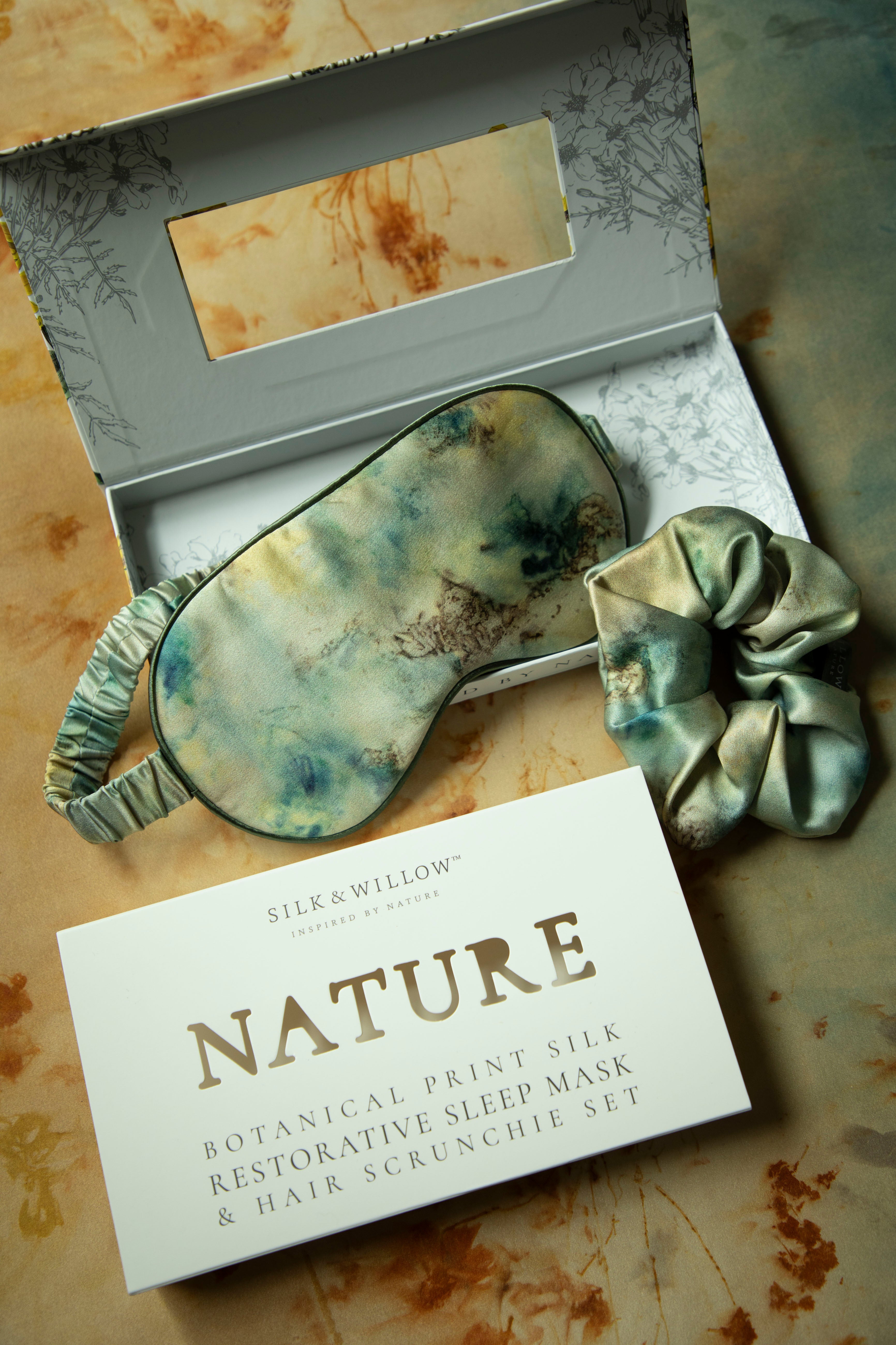 Silk & Willow Nature botanical print silk sleep mask and hair scrunchie set on a textured surface.
