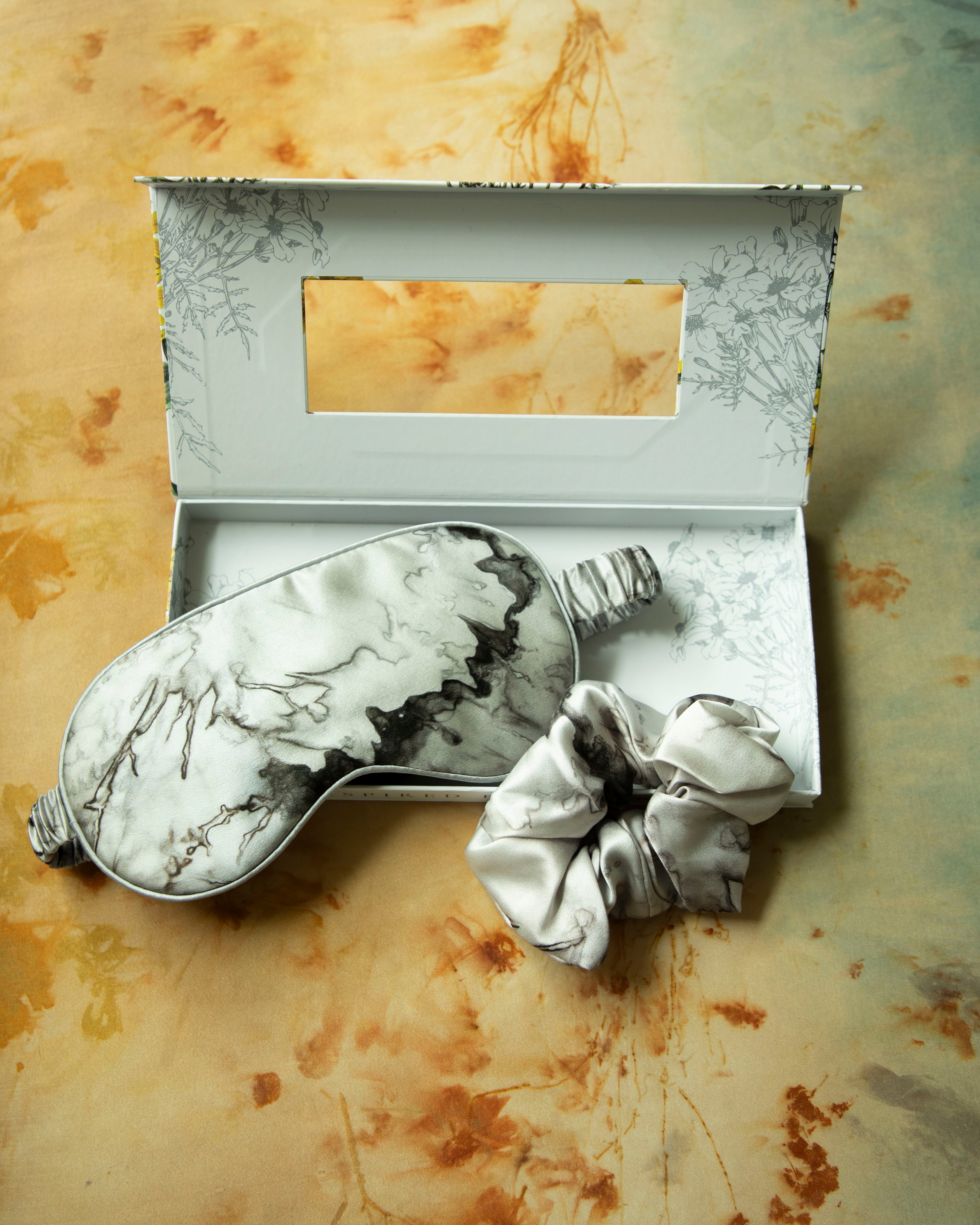 Marble-patterned eye mask and hair tie set on a textured beige background