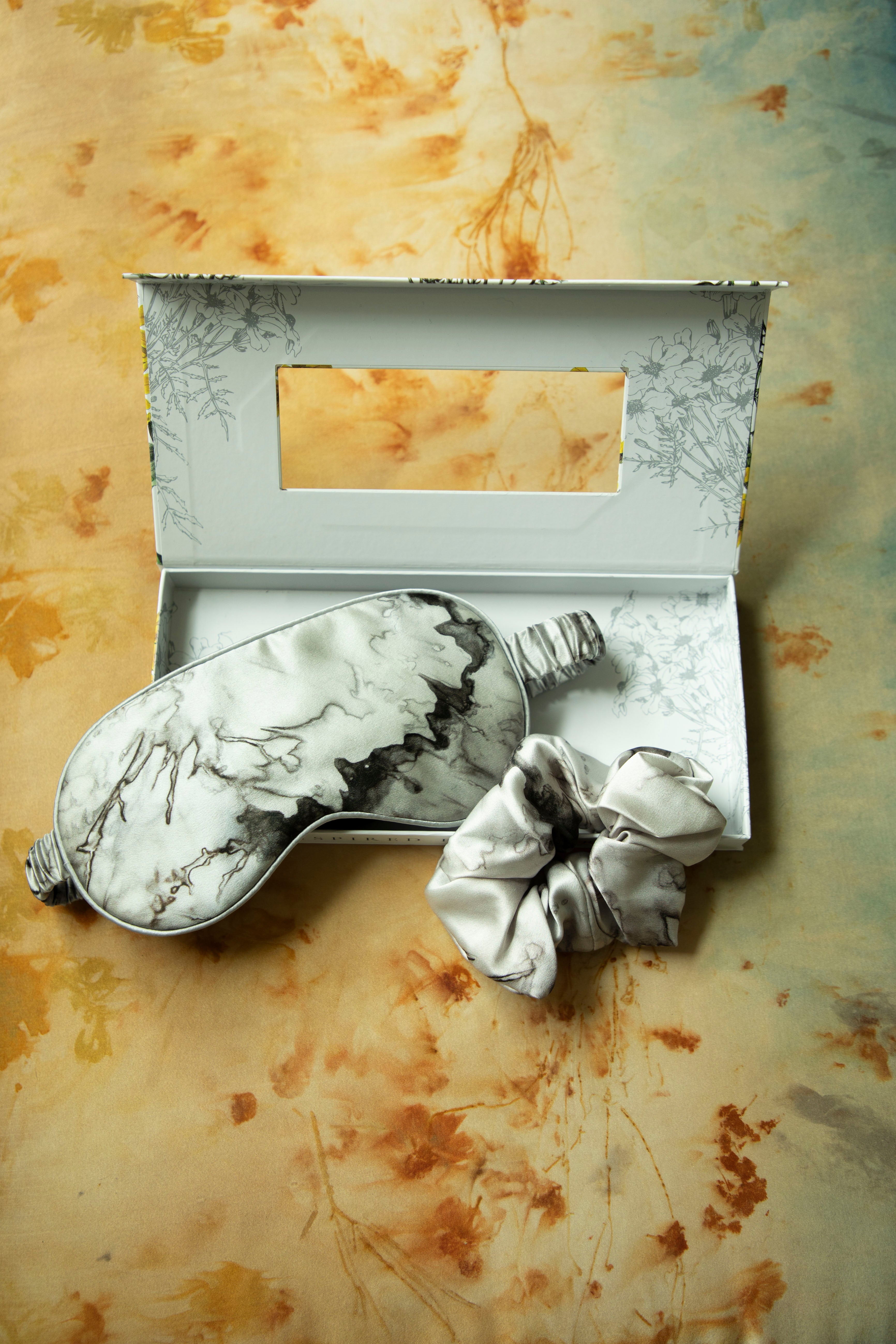 Marble-patterned eye mask and hair tie set on a textured beige background