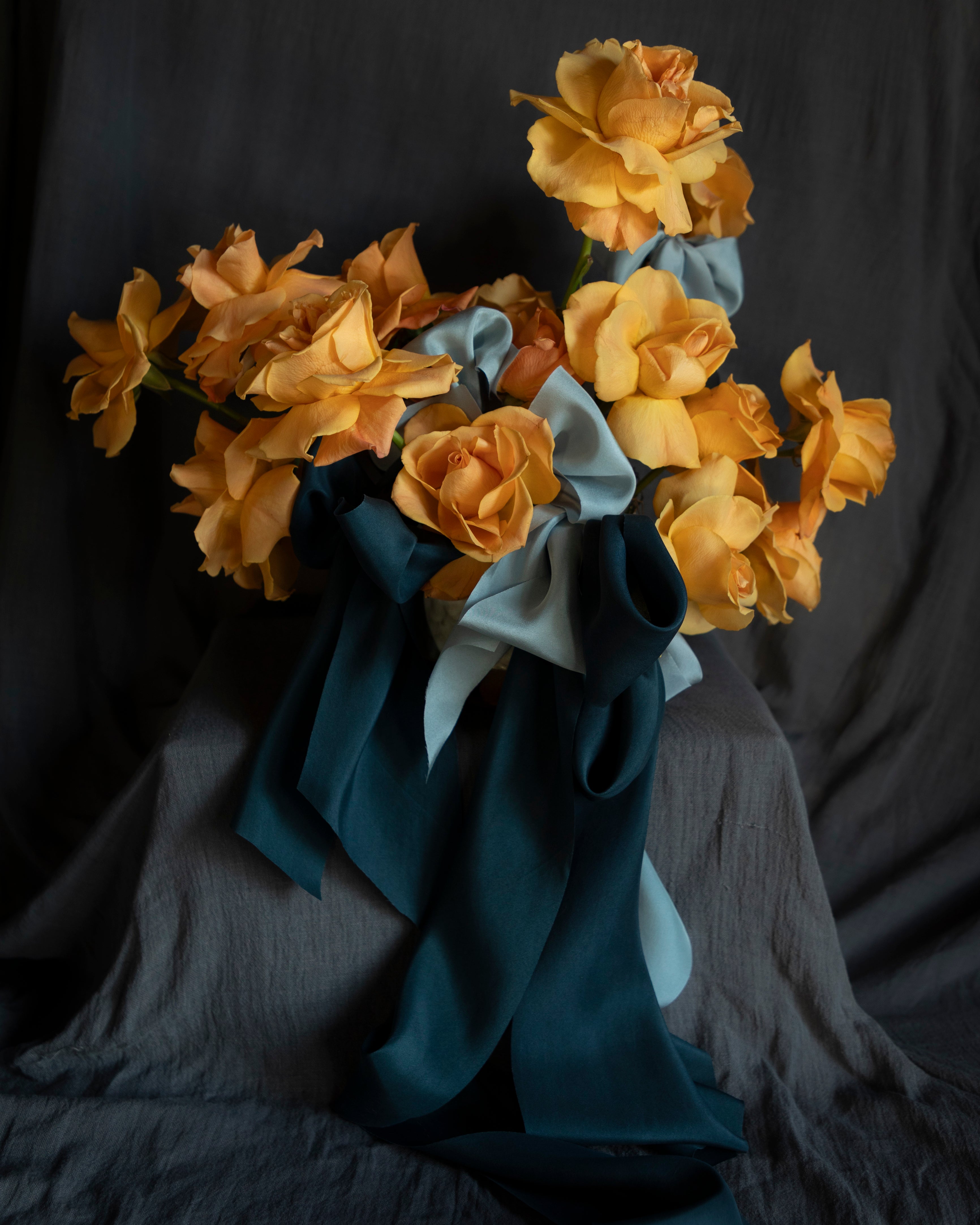 Bouquet of coral rose flowers wrapped with blue silk ribbon bows against a dark background